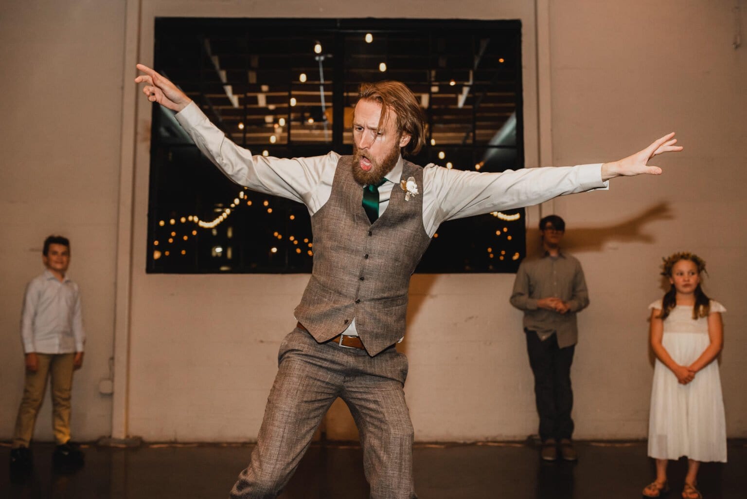 A man in a vest energetically dances at a party, with three children watching in the background. The lively scene captures the joy of the celebration in a way thats perfect for wedding photos at Castaway Portland.