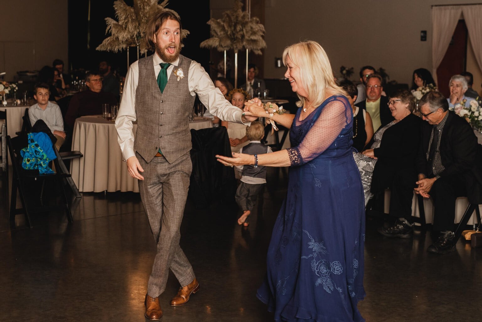 A man and woman joyfully dancing at an indoor event, while guests watch from their tables, captures a lively moment that could easily be part of wedding photos at Castaway Portland.