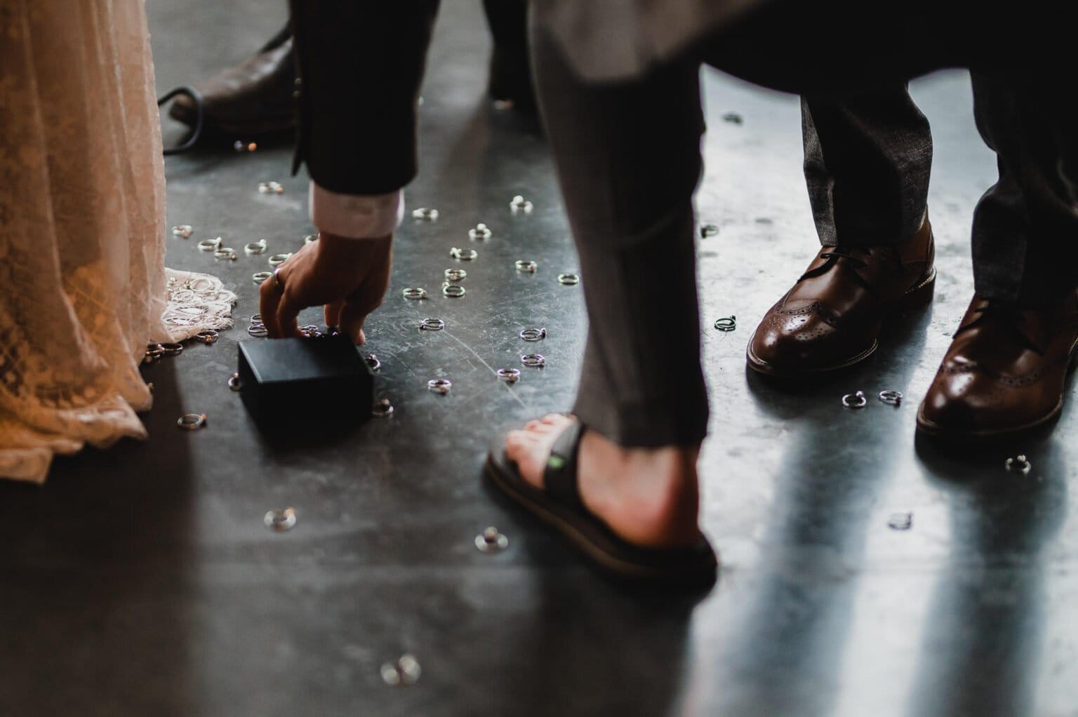 A person in a suit picks up a box from the floor, which is littered with bubbles. One is dressed in formal shoes while the other sports flip-flops, perhaps preparing for some unique wedding photos at Castaway Portland.