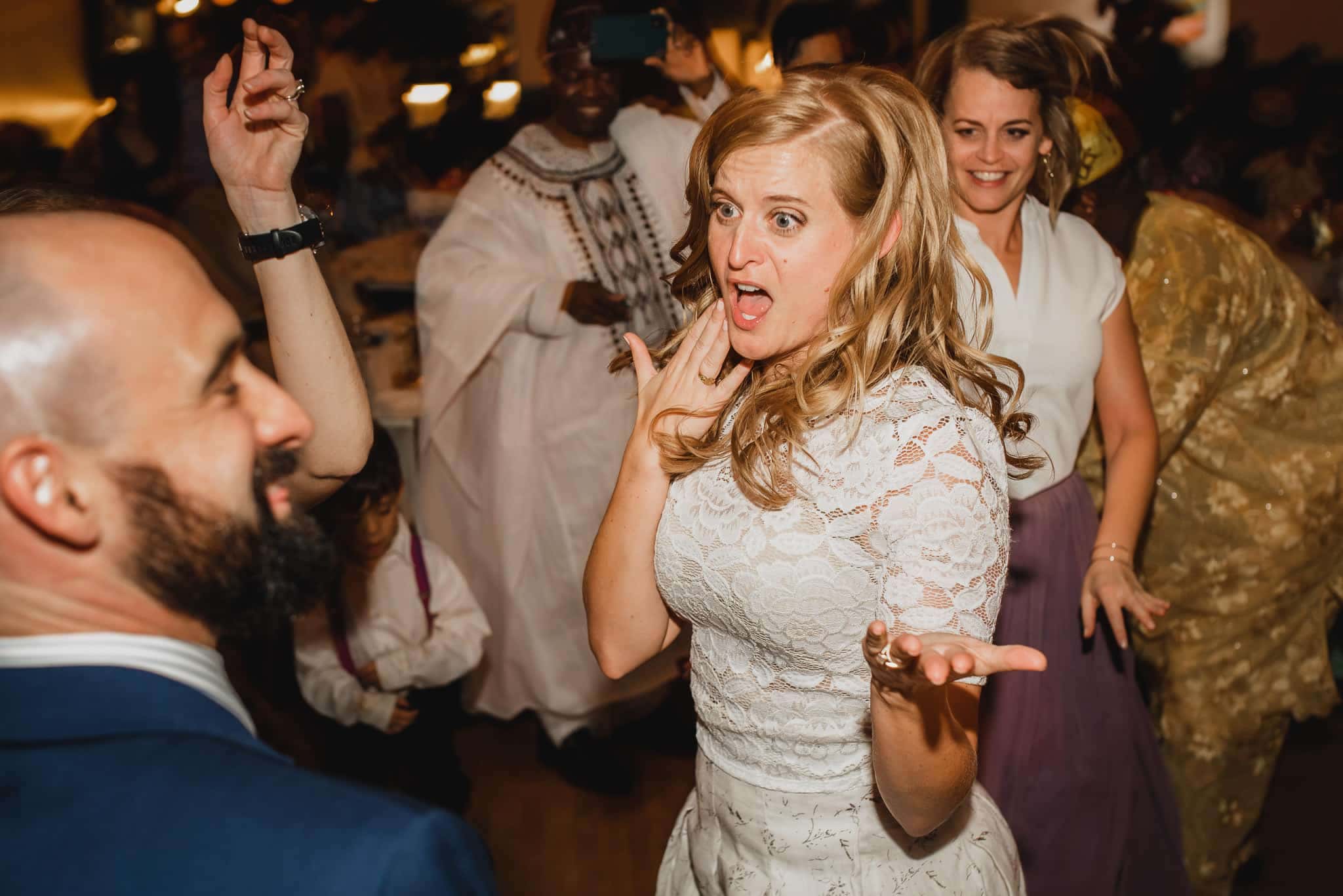 People dancing energetically at a lively wedding at the Evergreen, with a woman in a white dress expressing surprise and excitement.