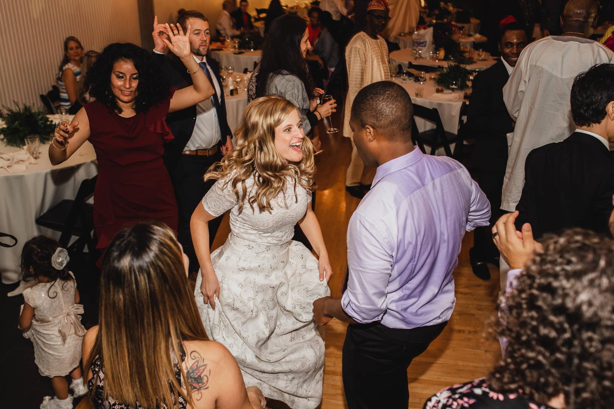 People dancing energetically at a wedding reception at the Evergreen, with tables and other guests in the background.