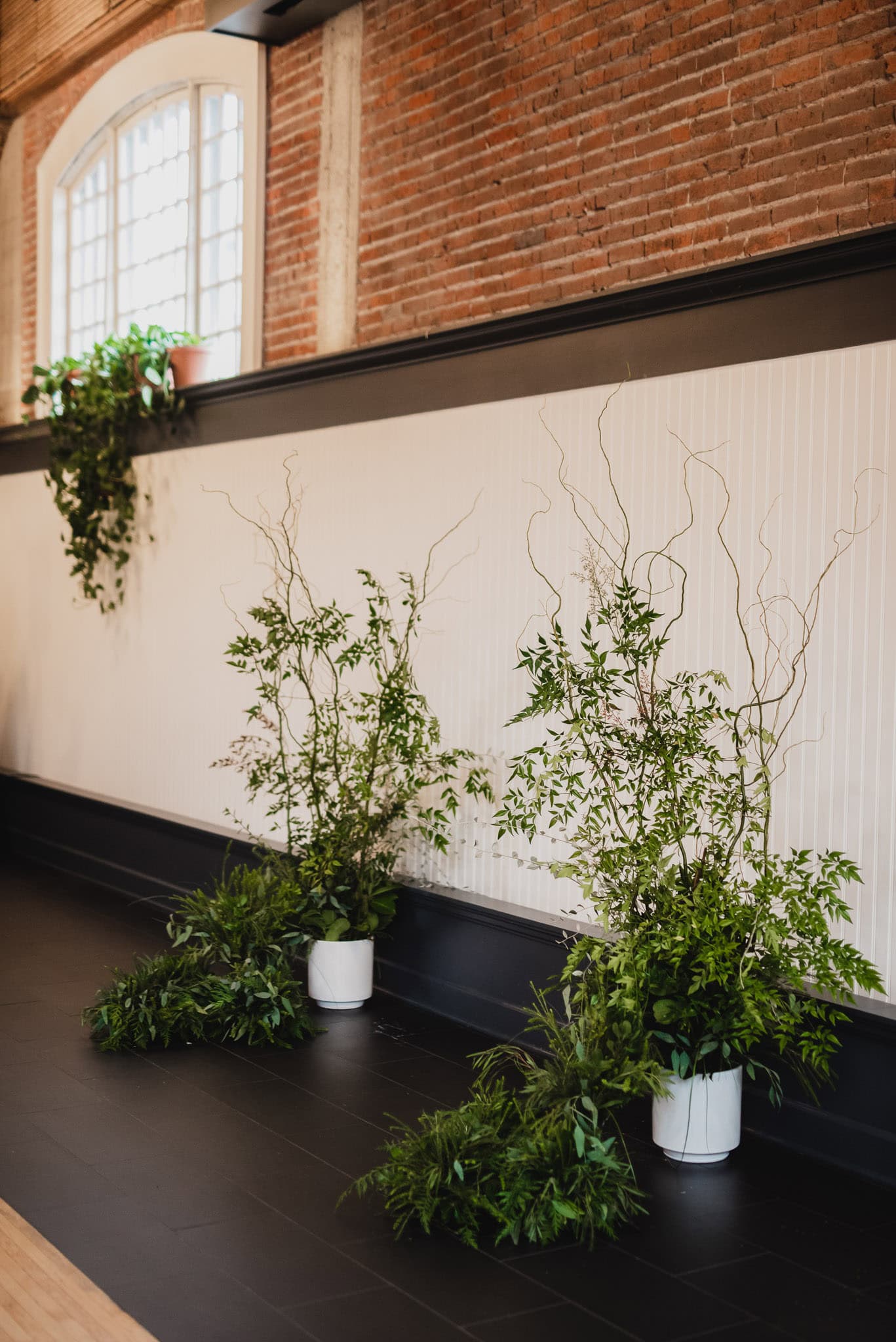 Green plants in white pots stand elegantly against a brick wall and large window in a modern interior space, perfectly setting the scene for a wedding at the Evergreen.