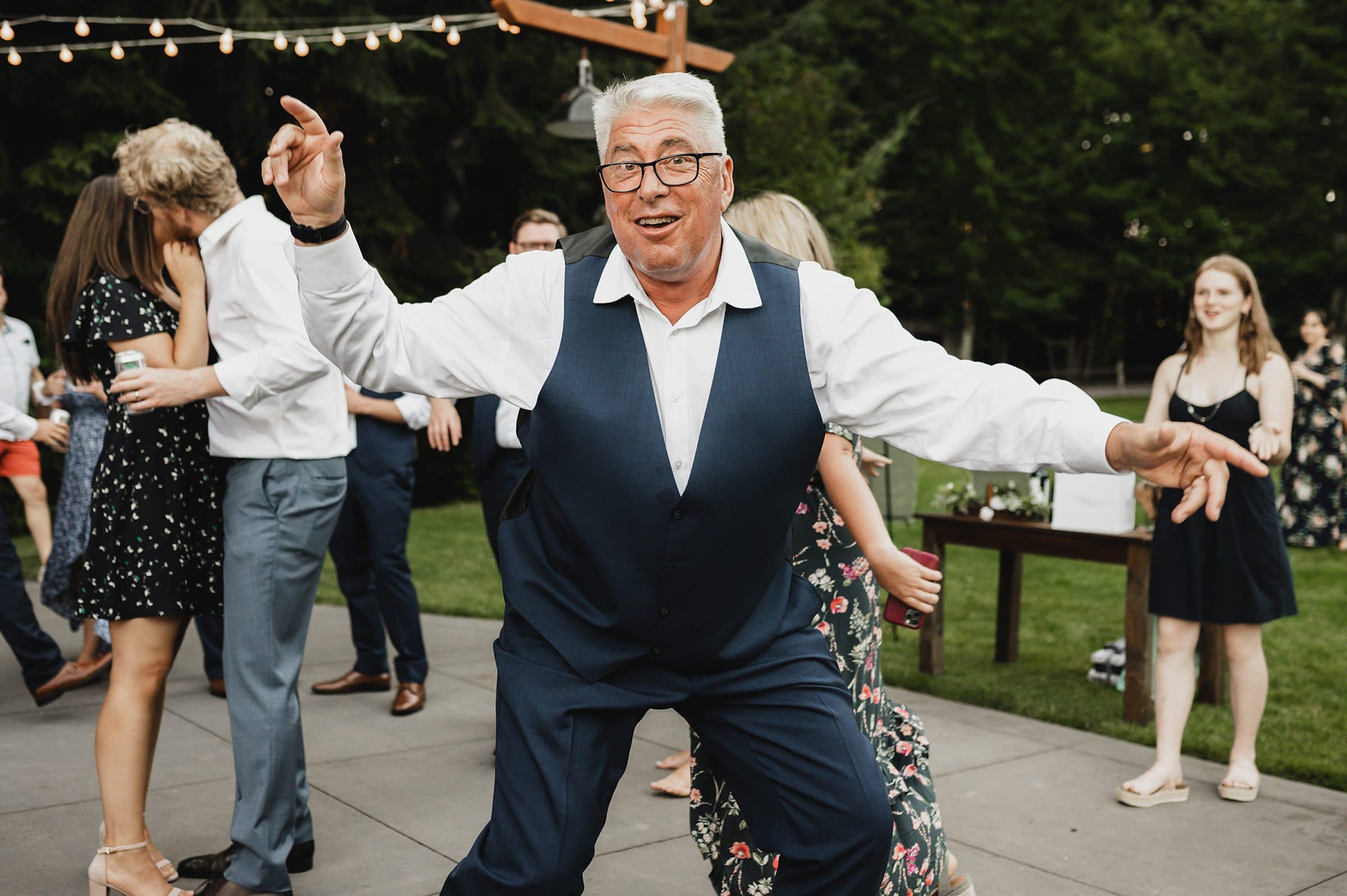 A man in a suit dances energetically at a Gorge Crest Vineyard wedding, surrounded by other joyful guests.