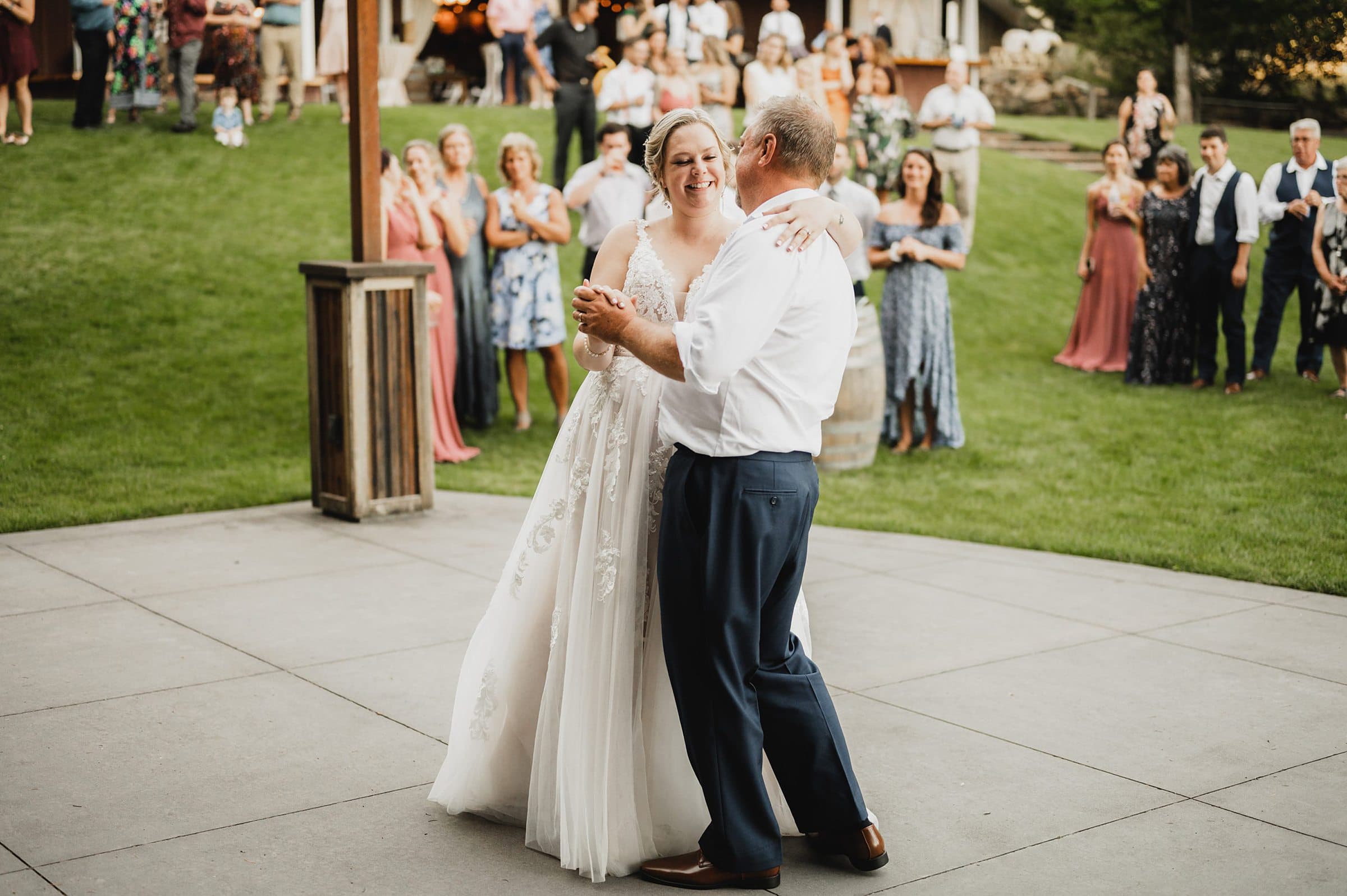 The bride and groom dance outside at their Gorge Crest Vineyard wedding, surrounded by smiling guests who watch and clap enthusiastically.