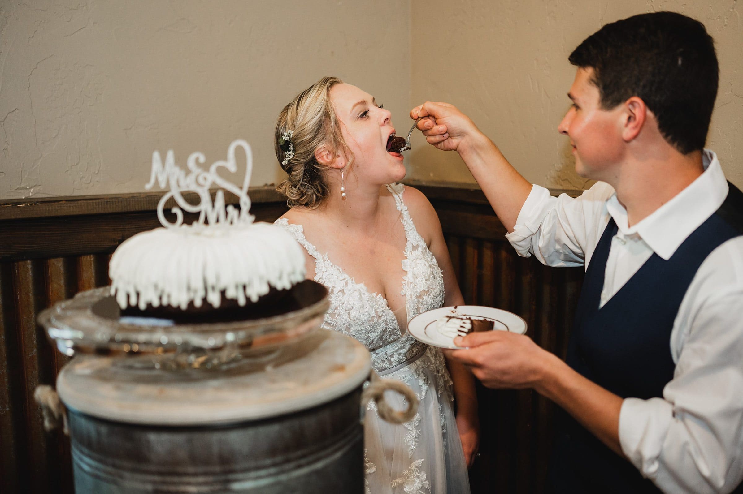 The bride and groom feed each other chocolate cake beside a beautifully decorated Mr. & Mrs. topper, captured perfectly in their wedding photos at Gorge Crest Vineyards.