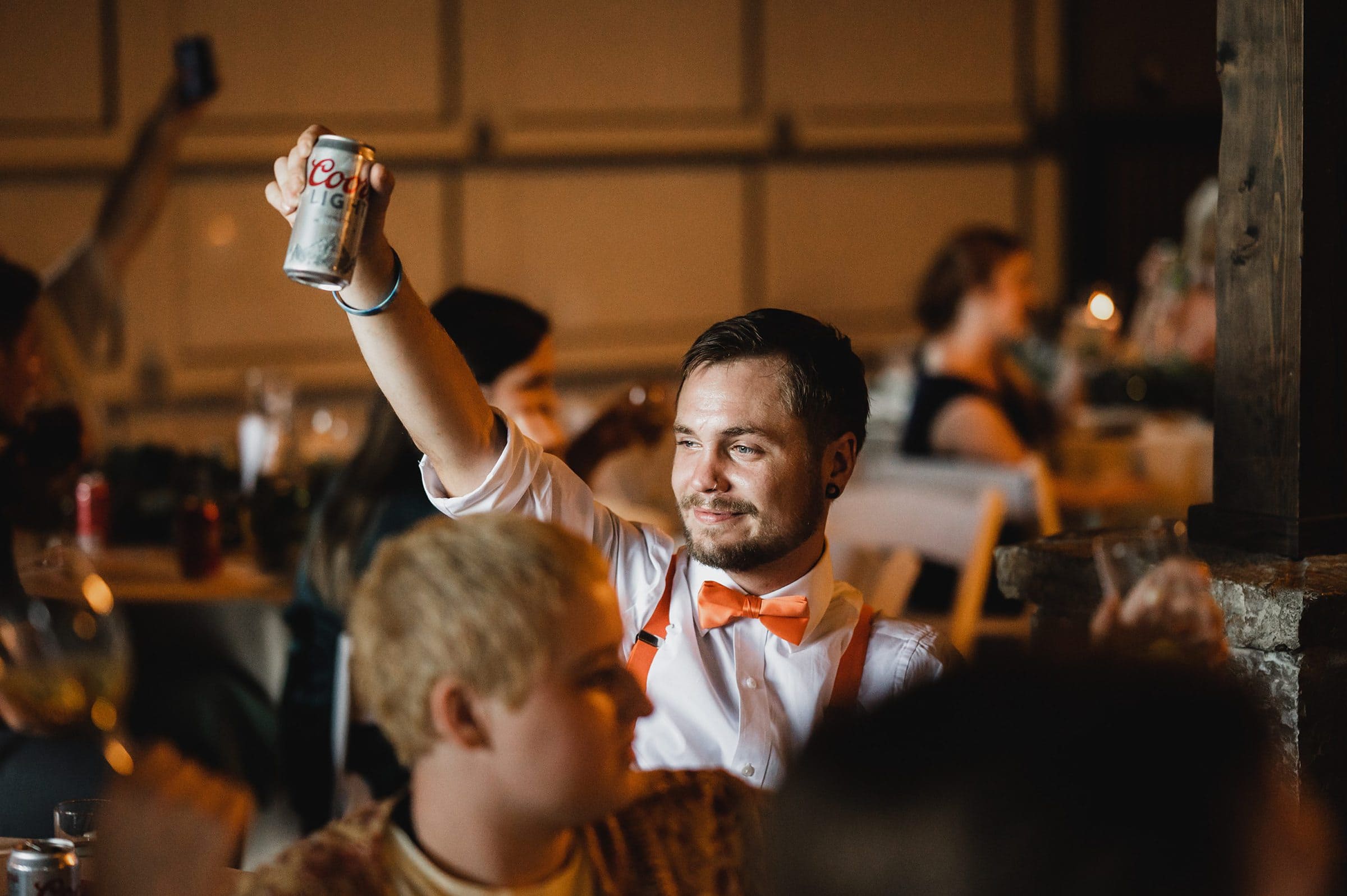 A man in an orange bow tie raises a Coors Light can at a social gathering, reminiscent of lively moments captured in Gorge Crest Vineyards wedding photos.