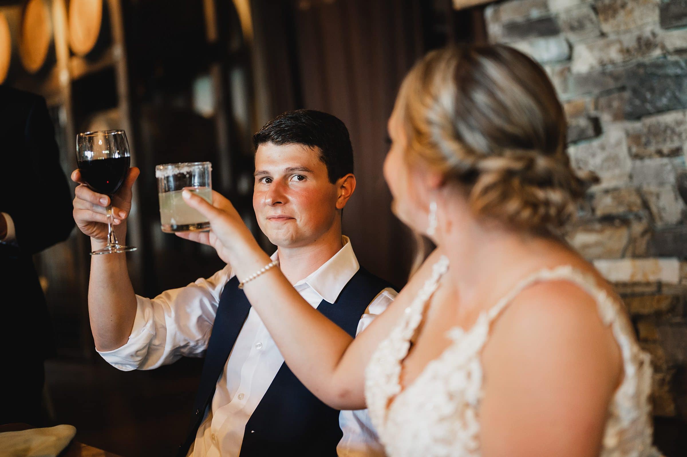 The bride and groom raise a toast with red wine and a cocktail in the charming setting of Gorge Crest Vineyards, creating memorable wedding photos.
