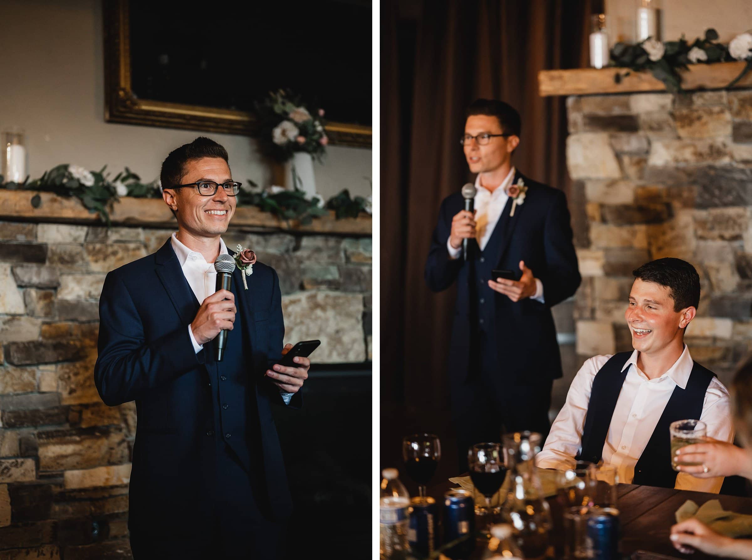 A man in a suit delivers a speech, while another man sits nearby, smiling. The indoor setting features a stone wall and candles, creating an elegant atmosphere reminiscent of a Gorge Crest Vineyards wedding.
