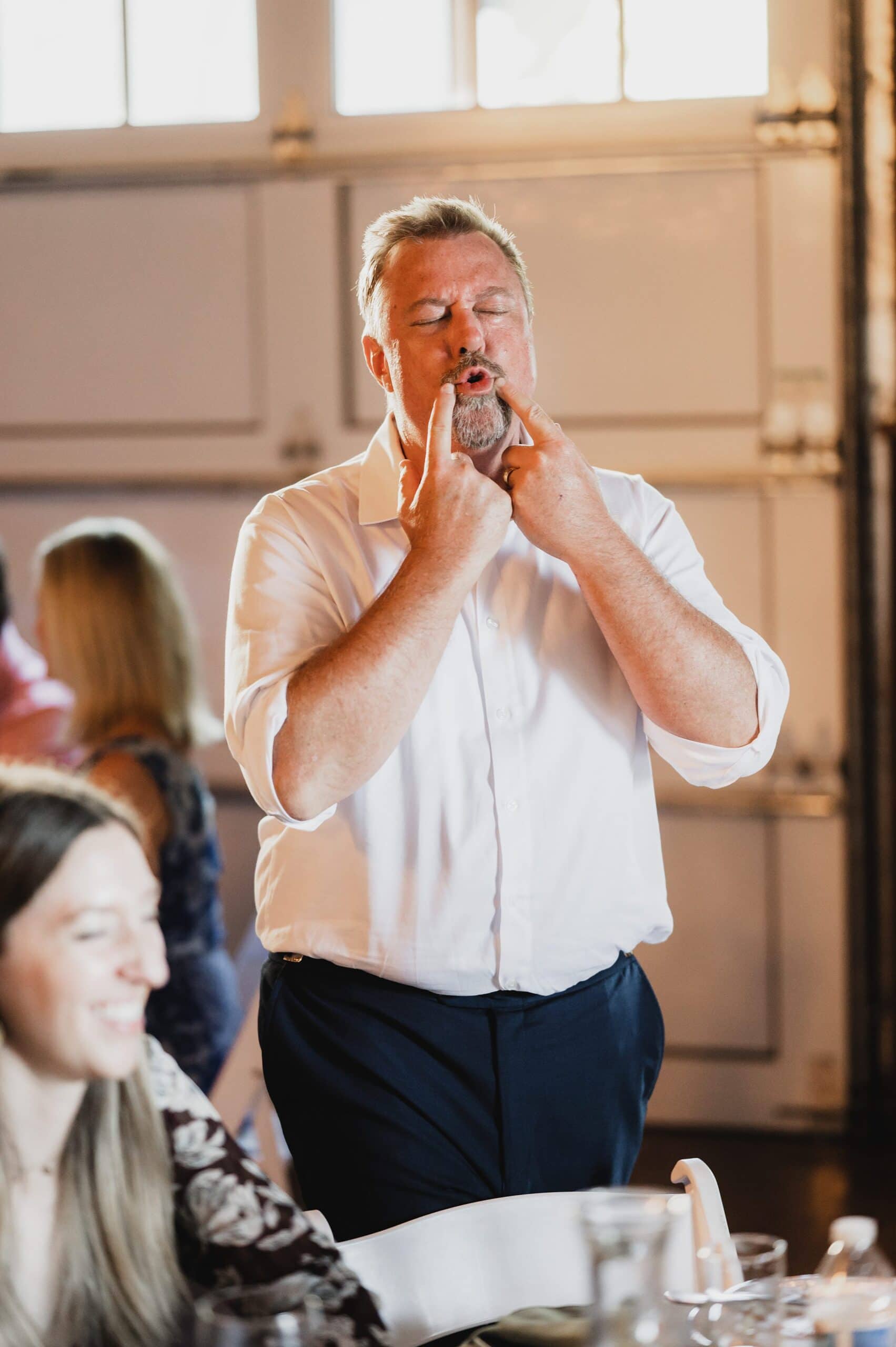 A man in a white shirt making a funny face while standing, with a woman smiling nearby, captures the joy of their special day during the wedding photos at Gorge Crest.