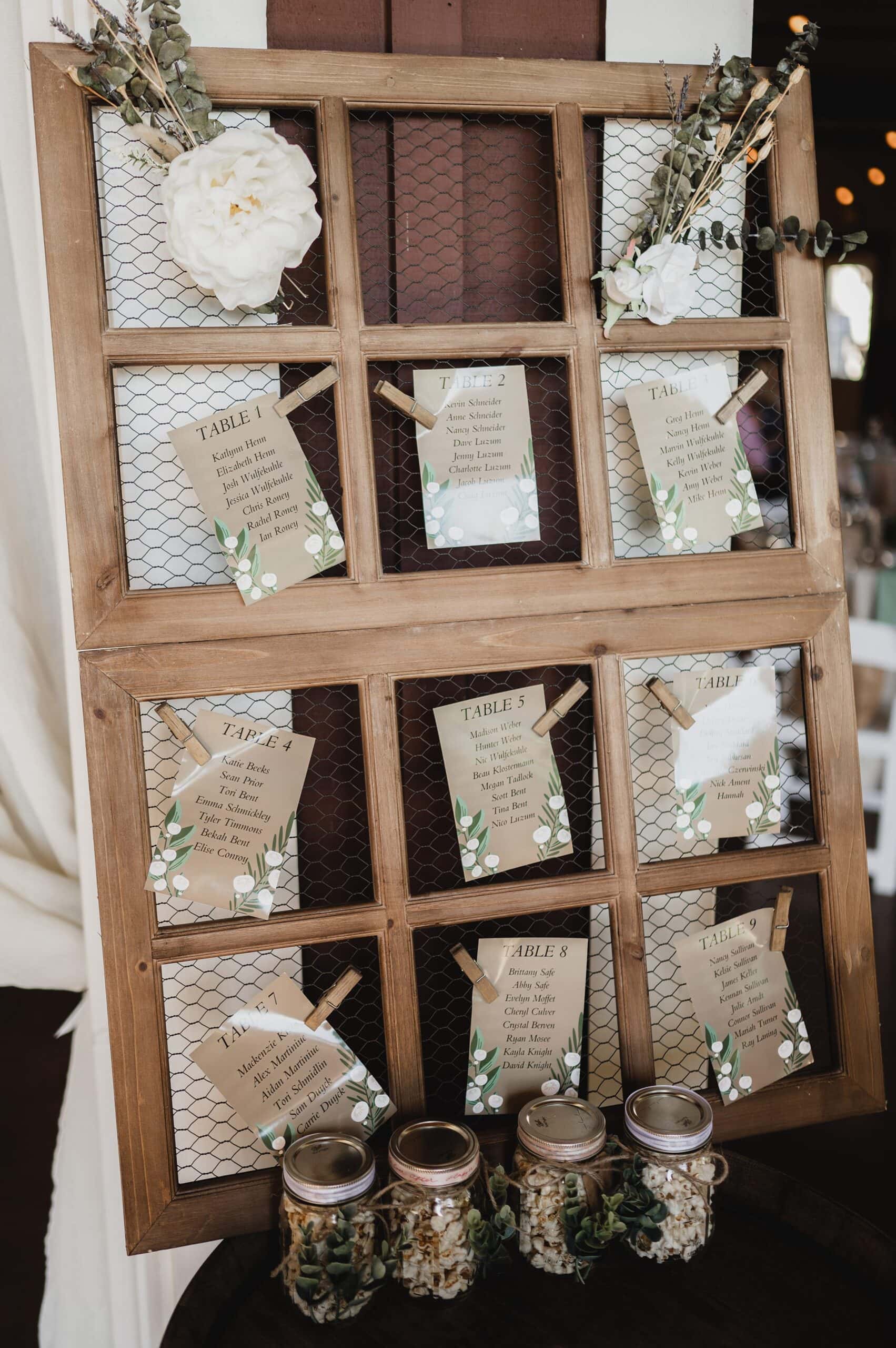 A rustic seating chart display at Gorge Crest Vineyards, adorned with floral accents and mason jars, features cards for different tables. Perfect for capturing memorable wedding photos!.