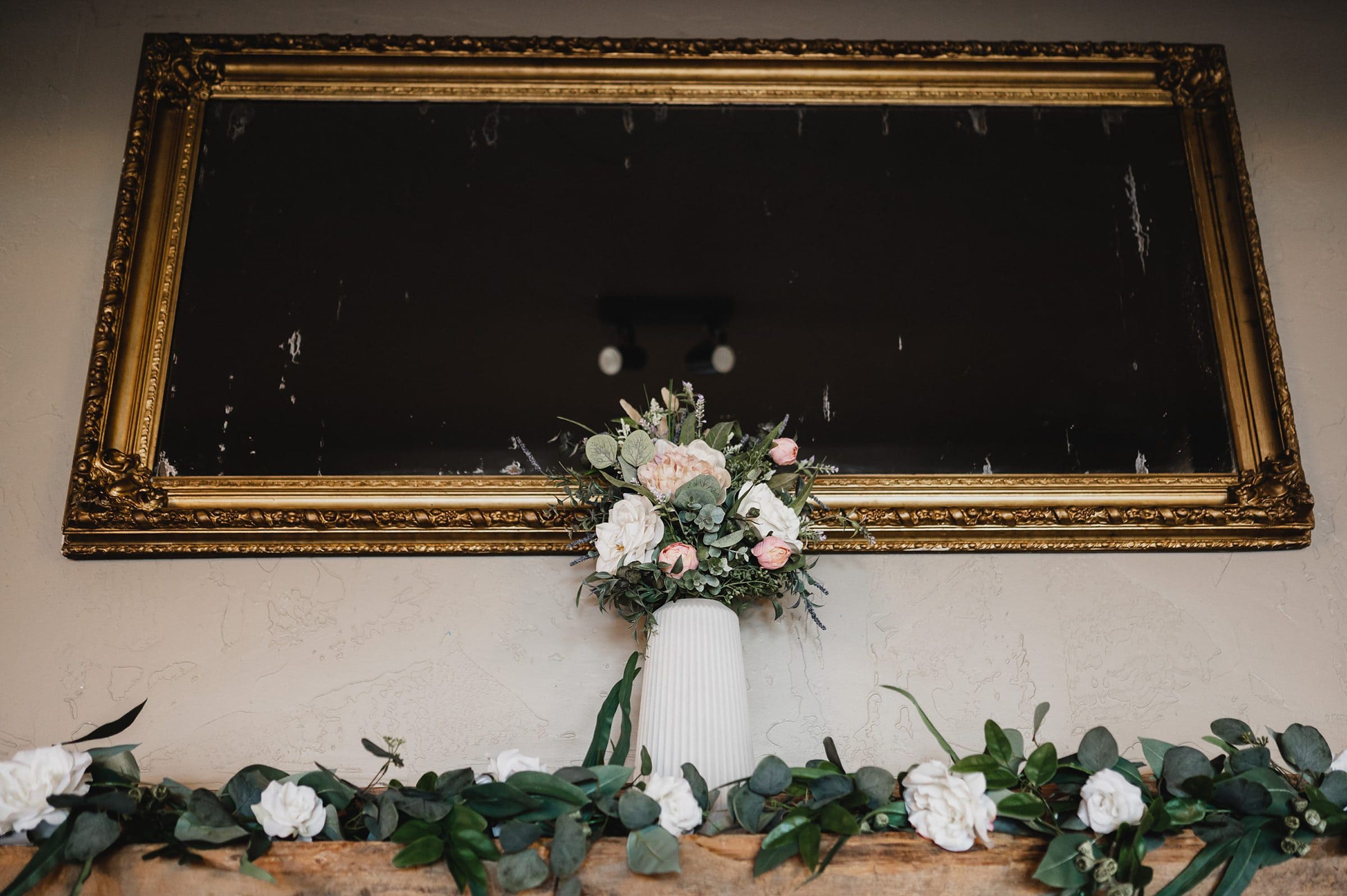 A gold-framed mirror elegantly sits above the mantel, adorned with a charming floral vase and a lush greenery garland. This idyllic setting is perfect for capturing memorable Gorge Crest Vineyard wedding photos.
