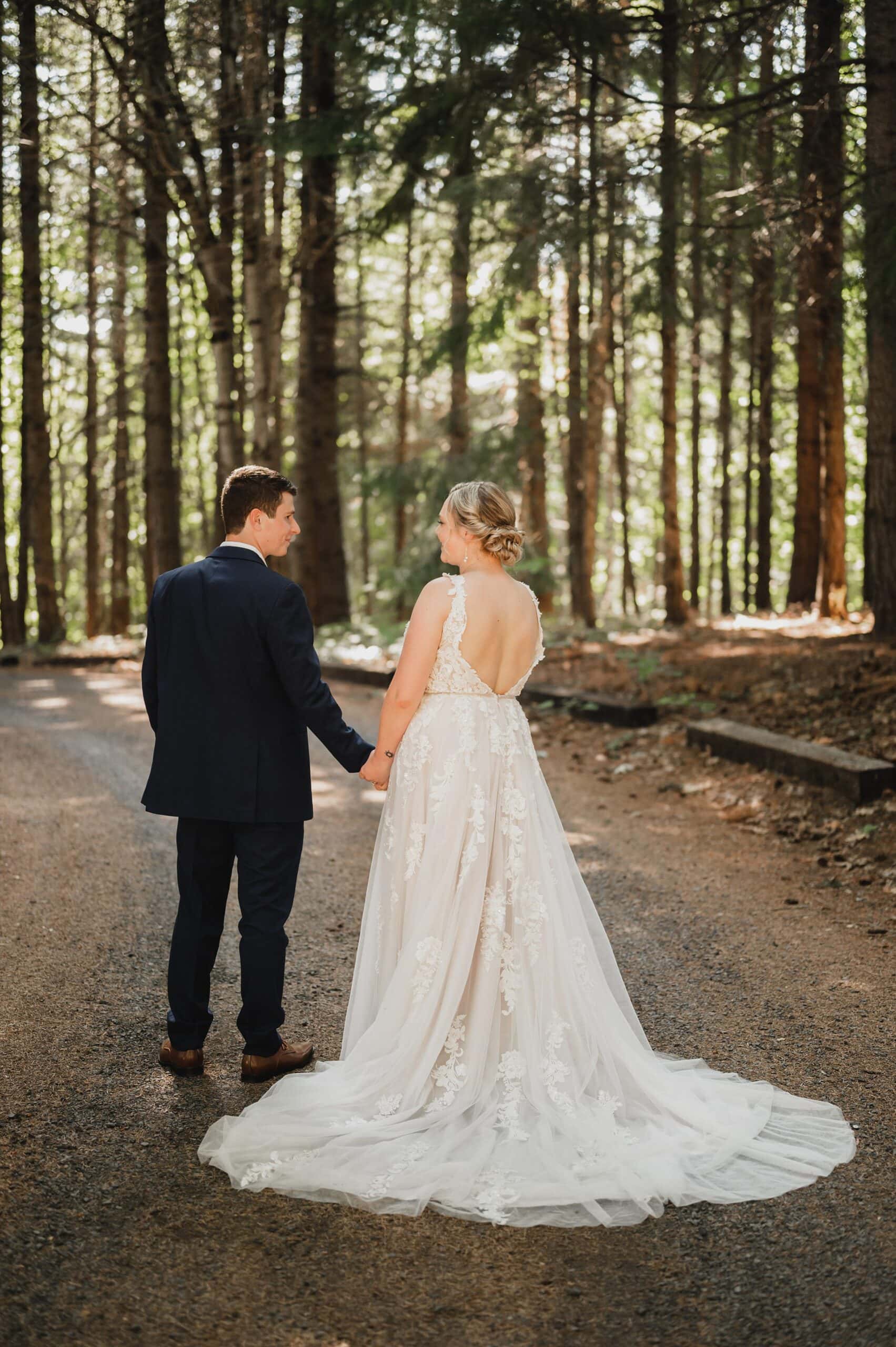 The bride and groom hold hands, gracefully walking on a forest path with sunlight filtering through the trees. This moment is captured beautifully as part of their Gorge Crest Vineyards wedding photos, where nature adds a touch of enchantment to their special day.