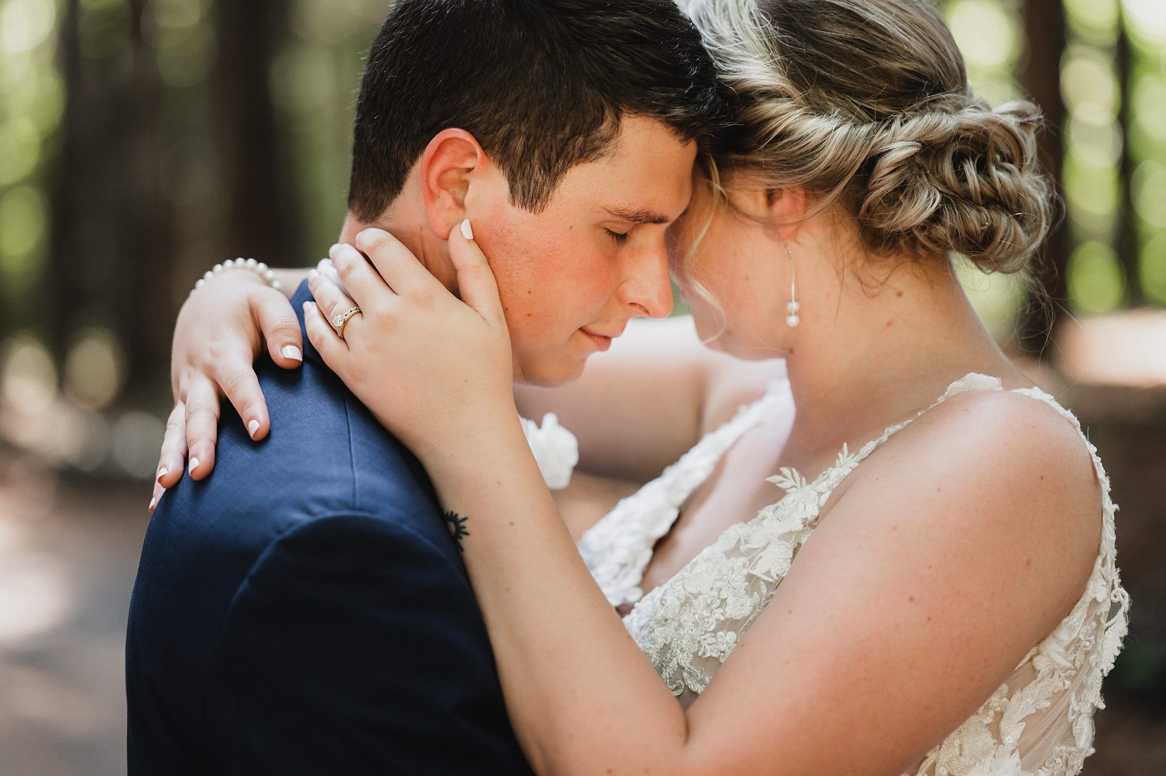 The couple, dressed in formal attire, embrace closely with eyes closed against the blurred backdrop of a forest, capturing the romance and serenity of a Gorge Crest Vineyard wedding.