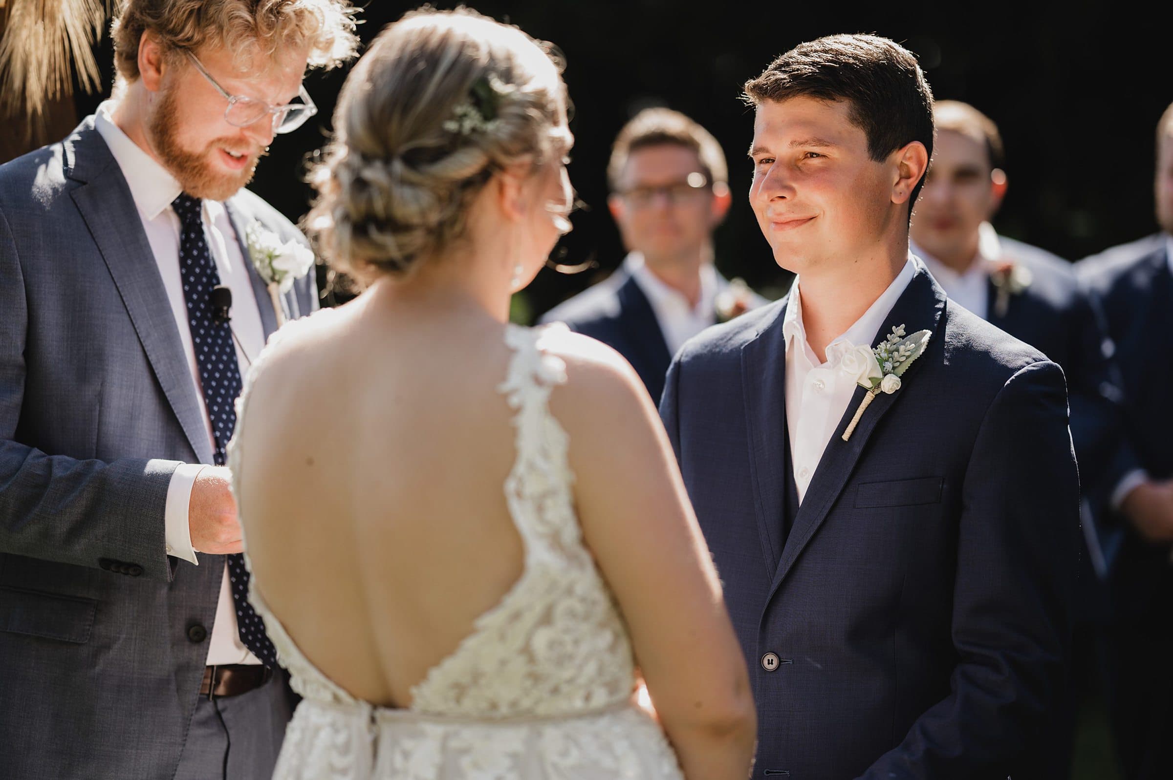 The couple gazes at each other during their ceremony at Gorge Crest Vineyards, with the officiant standing nearby, all in formal attire.