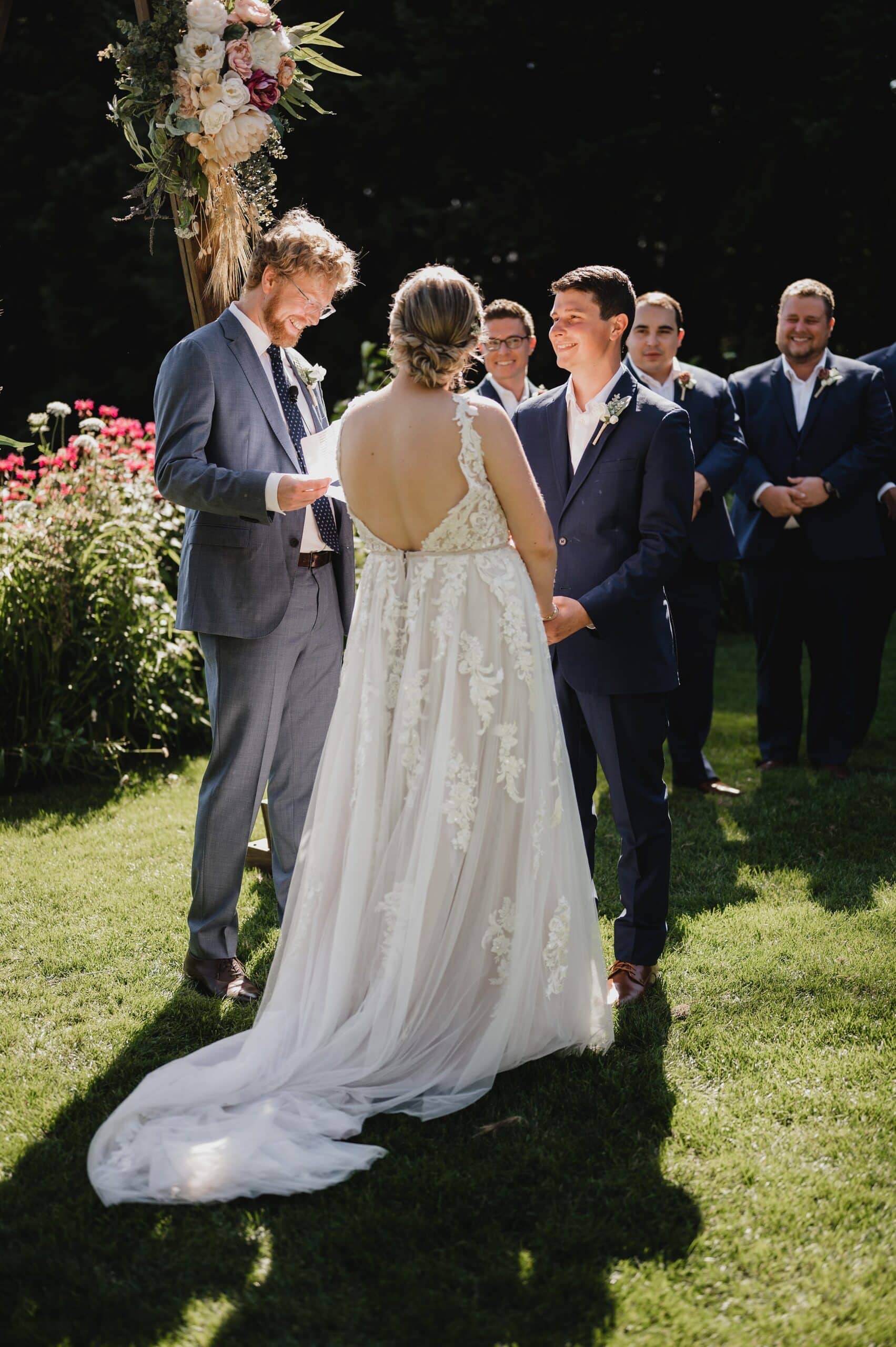 At Gorge Crest Vineyards, the bride and groom exchange vows under a clear sky, with a person officiating and guests gathered in the background for this beautiful outdoor ceremony.