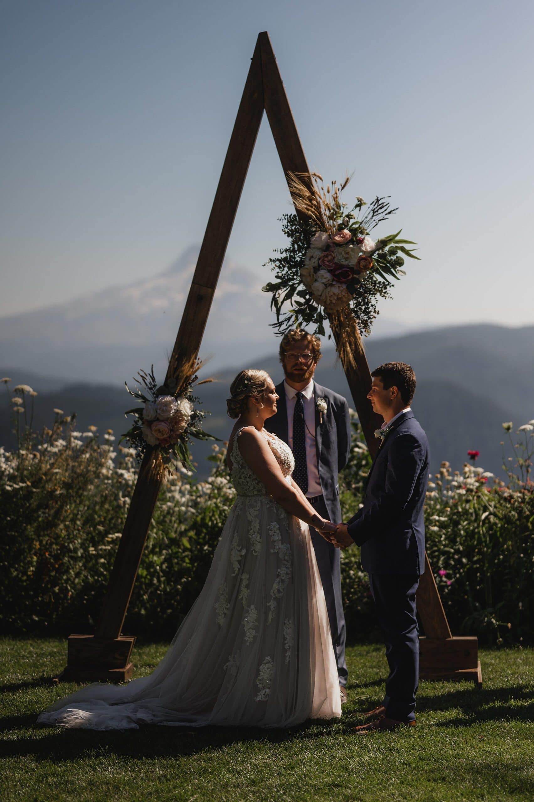 A couple stands before a triangle arch at their Gorge Crest wedding, with majestic mountains forming a stunning backdrop.