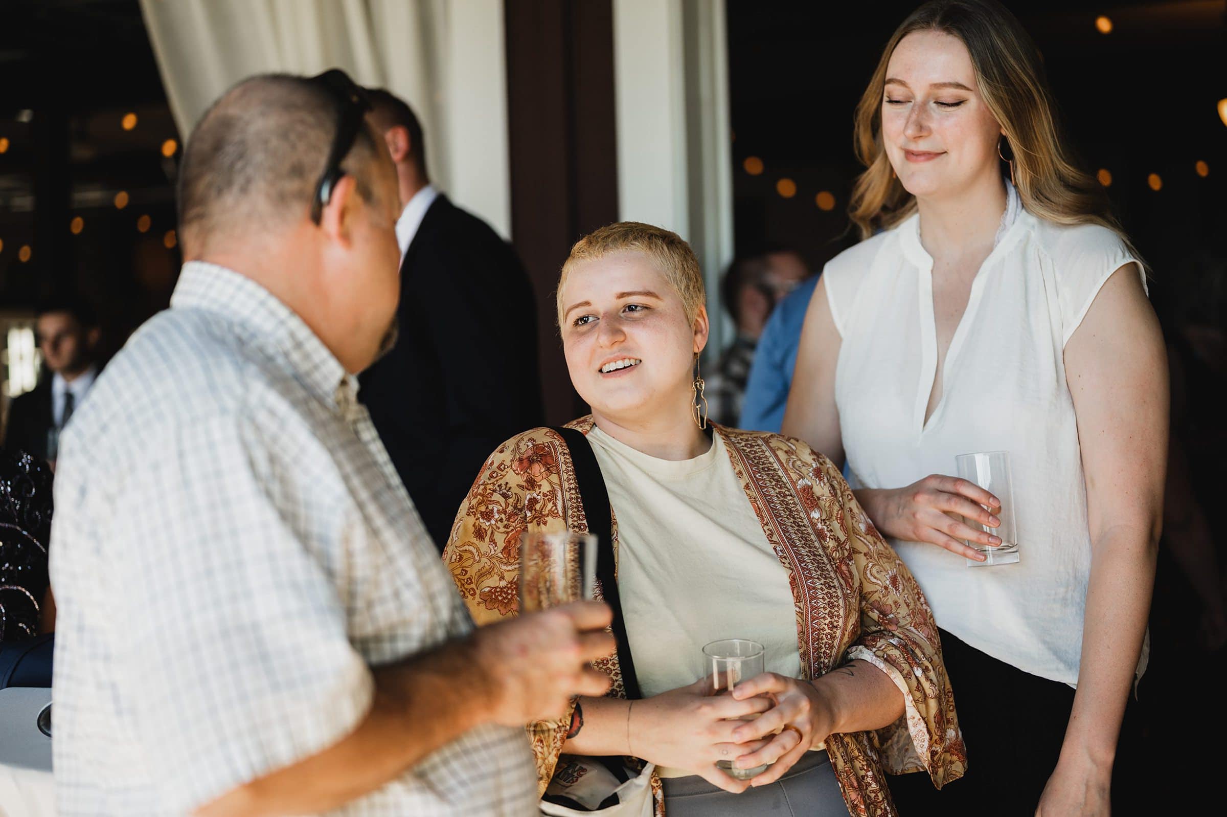 At a Gorge Crest Vineyards event, three people socialize indoors, holding drinks and smiling in casual attire.