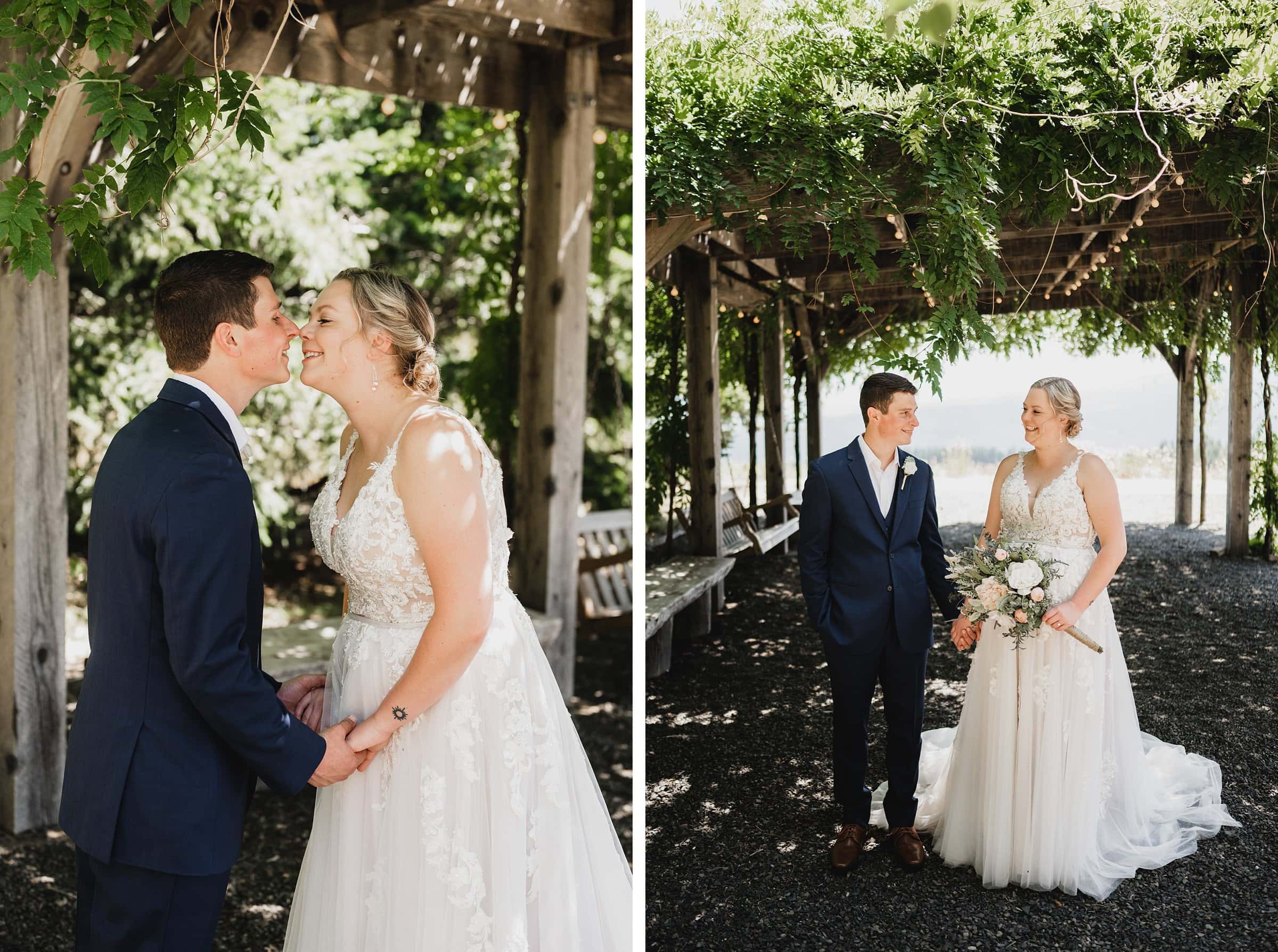 A couple in wedding attire kisses and holds hands under a pergola adorned with greenery. They are surrounded by the natural beauty of Gorge Crest Vineyards, creating a picturesque and romantic scene.