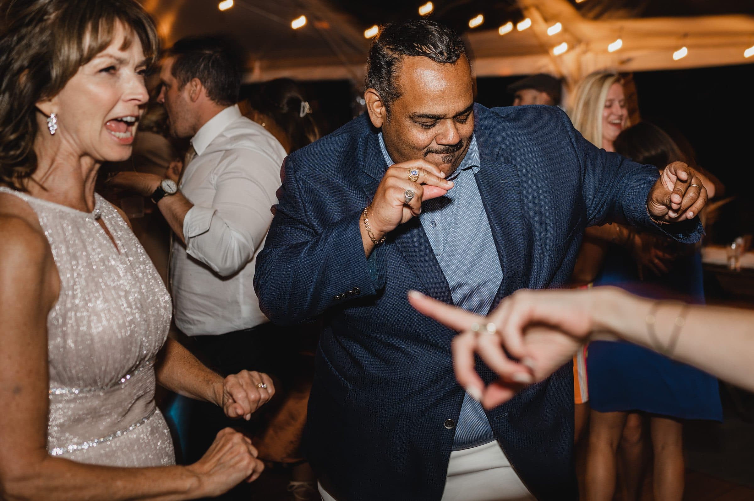 People dancing enthusiastically at a party under string lights, with one man in a blue blazer enjoying the music. It feels like a scene straight out of wedding photos at The Griffin House, where joyful moments are captured flawlessly.