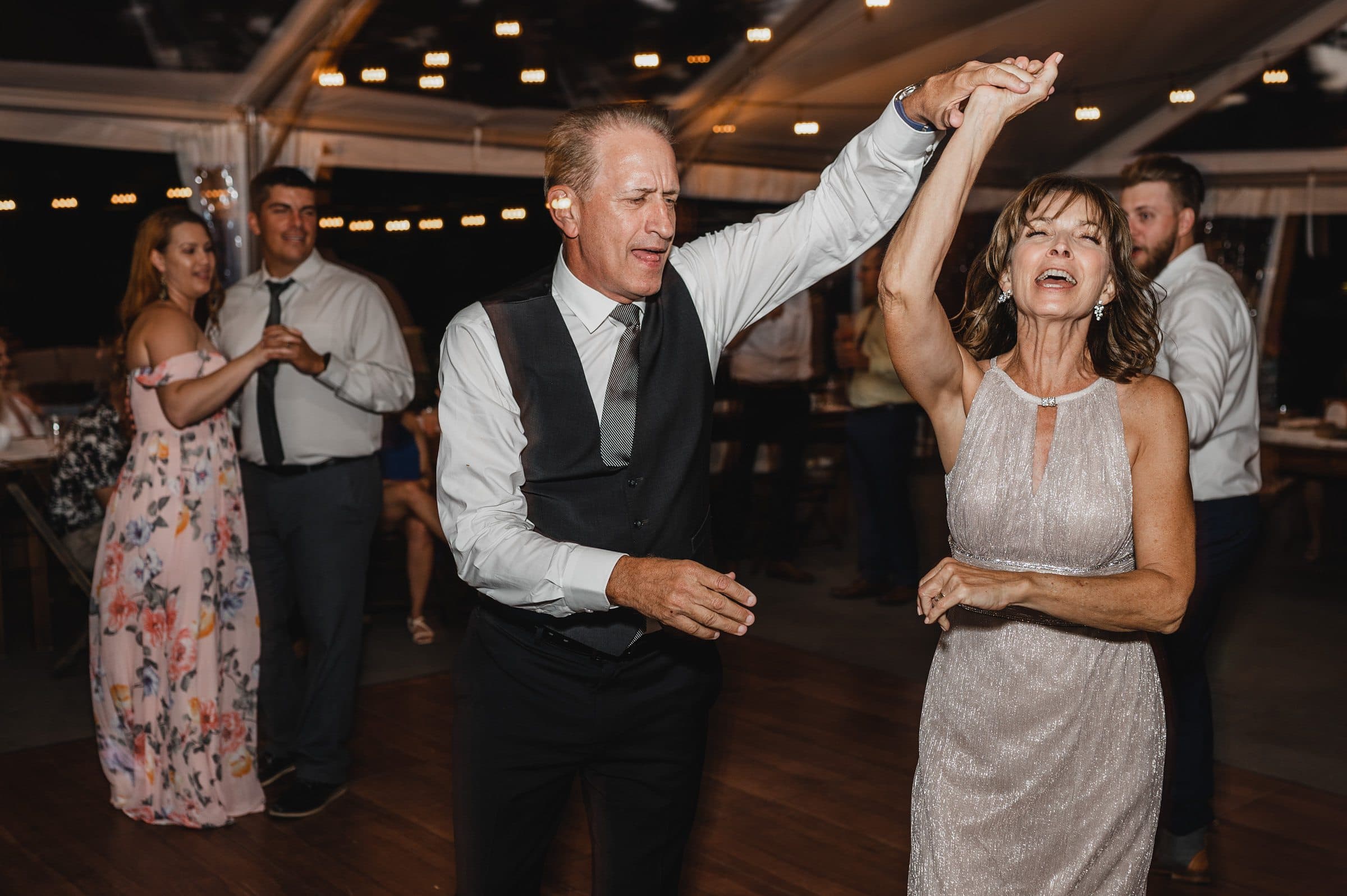 A man and woman are joyfully dancing at an event, with other attendees visible in the background, capturing the lively spirit of wedding photos at The Griffin House.