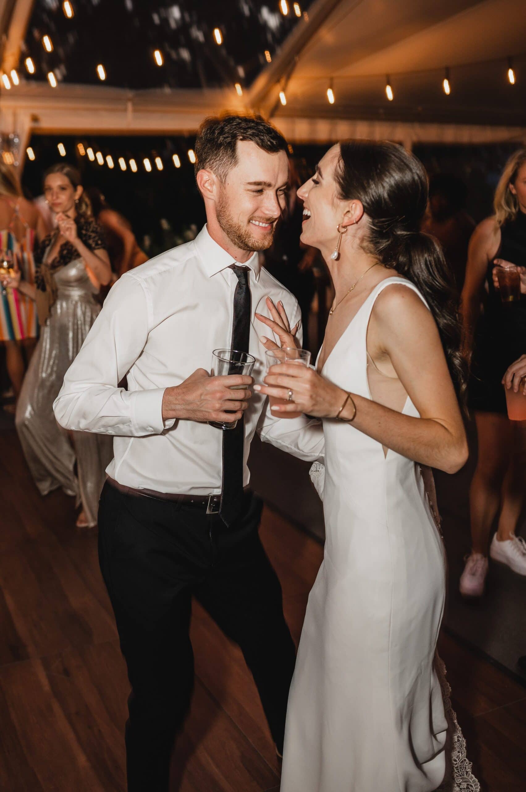 The bride and groom are all smiles as they dance together at a wedding reception under string lights, capturing perfect wedding photos at The Griffin House.