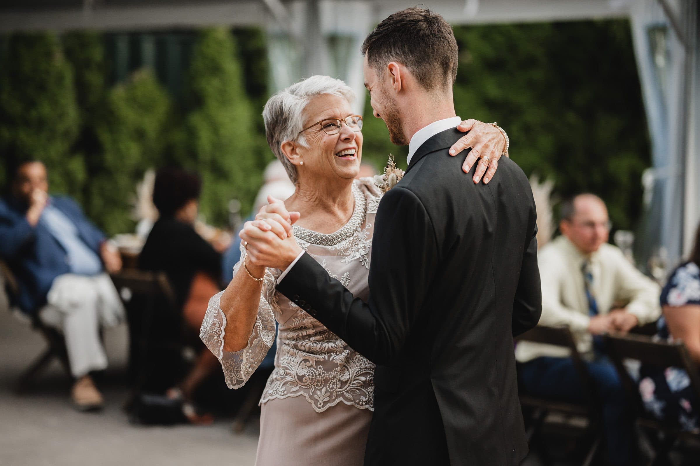 An elderly woman and a man are dancing together outdoors at The Griffin House, where wedding photos capture the joyous celebration.