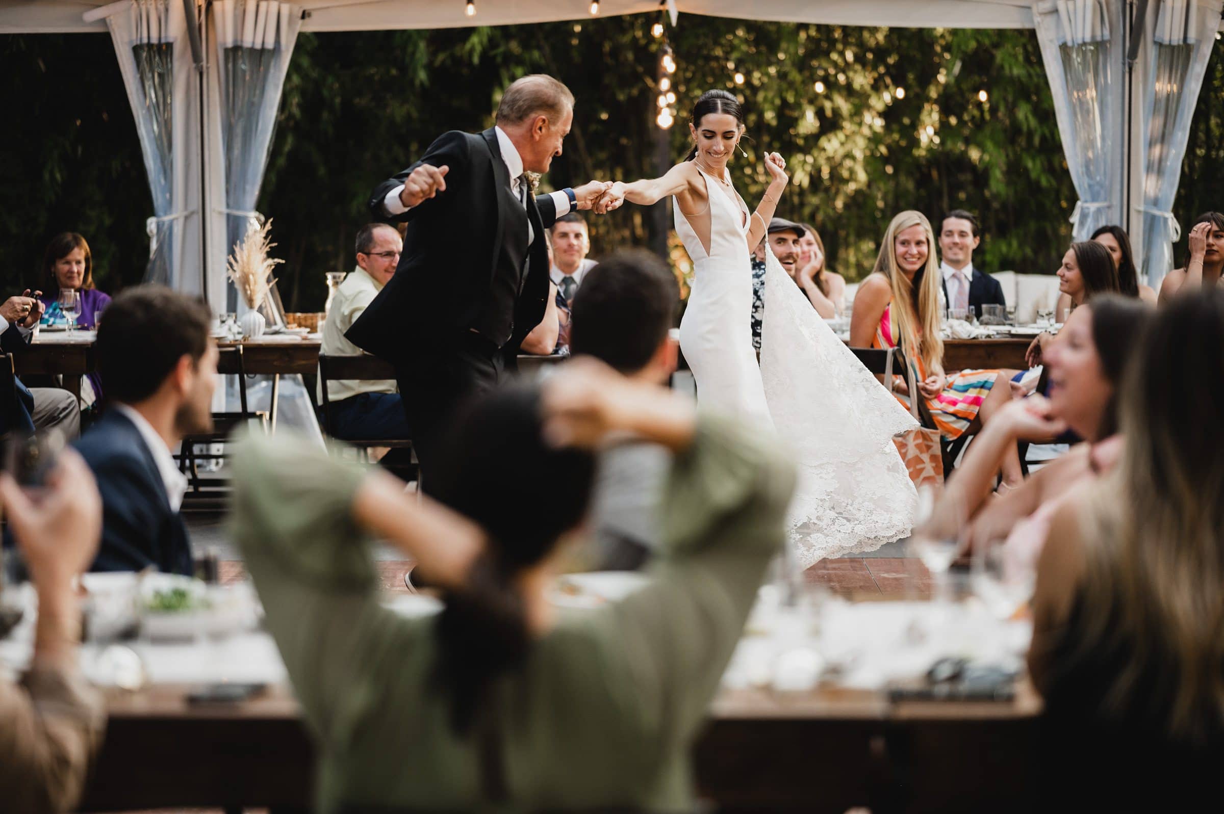 The bride and her father share a dance at an outdoor wedding reception at The Griffin House, surrounded by guests capturing the moment in wedding photos.