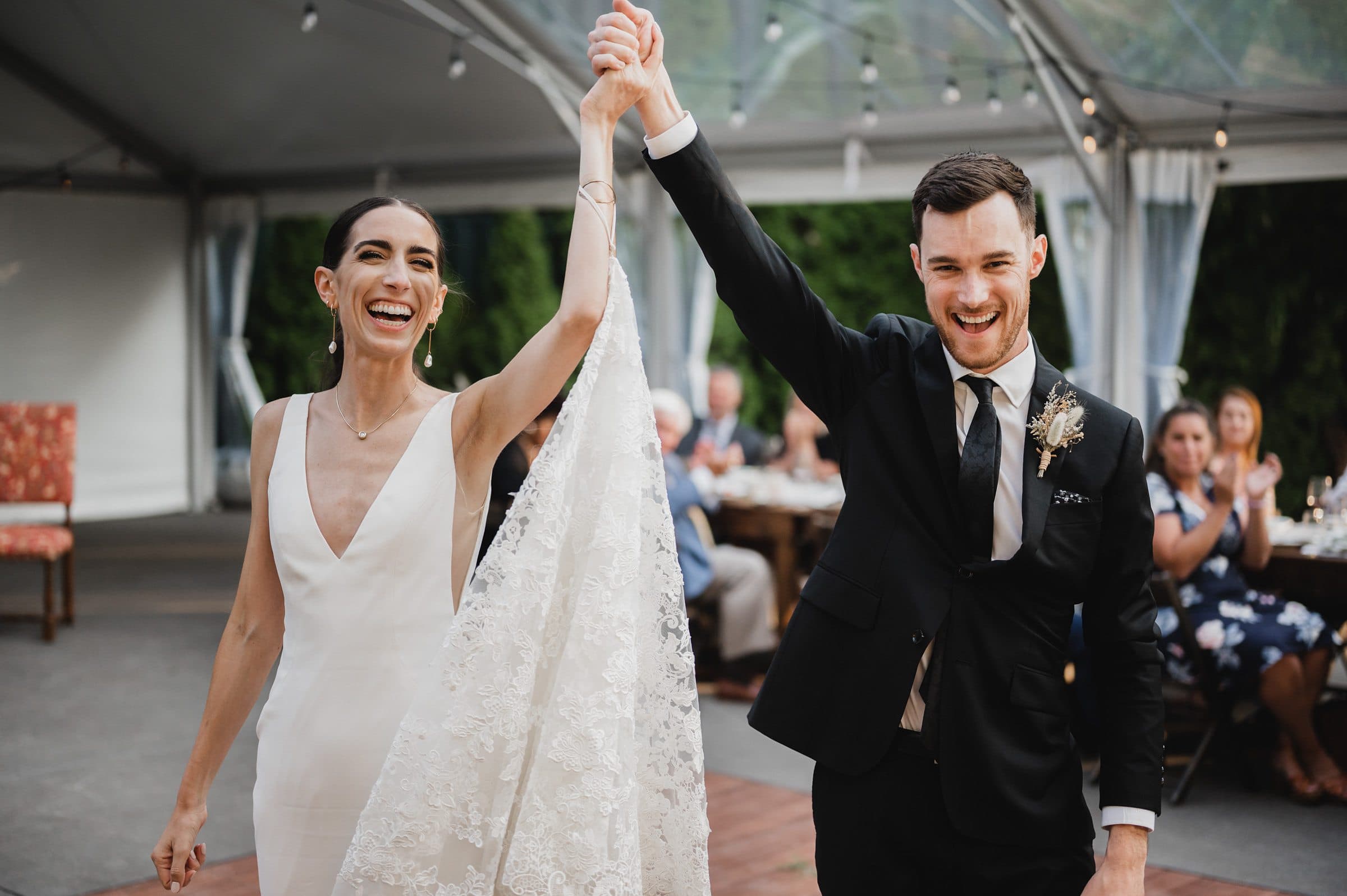 The bride and groom joyfully raise their hands under a tent, celebrating with guests in the background. This moment was perfectly captured among the stunning views of wedding photos at The Griffin House.