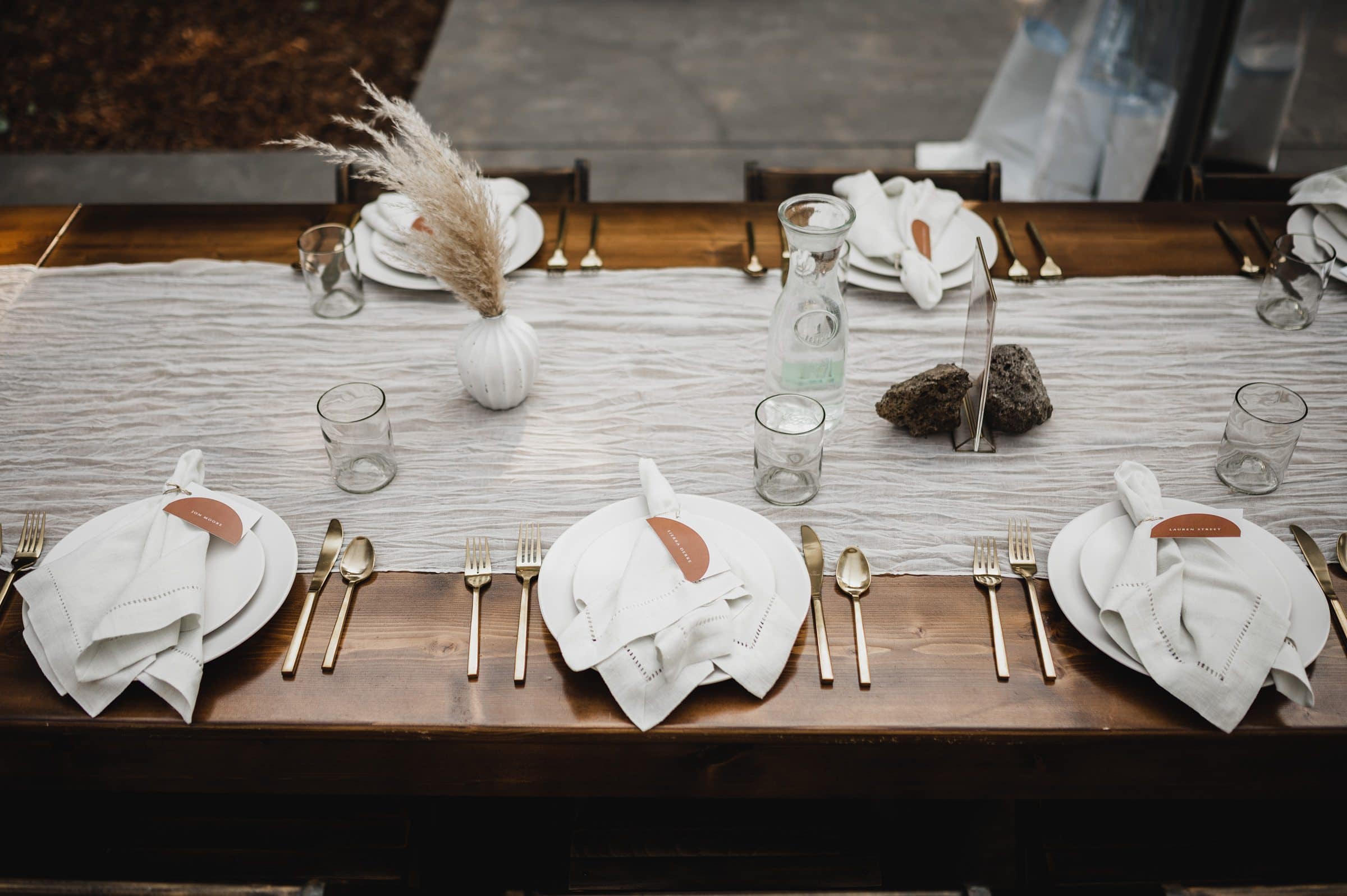 A rustic table setting features plates, cutlery, glasses, napkins, a centerpiece, and decorative rocks on a wooden table. Perfect for capturing elegant wedding photos at The Griffin House.