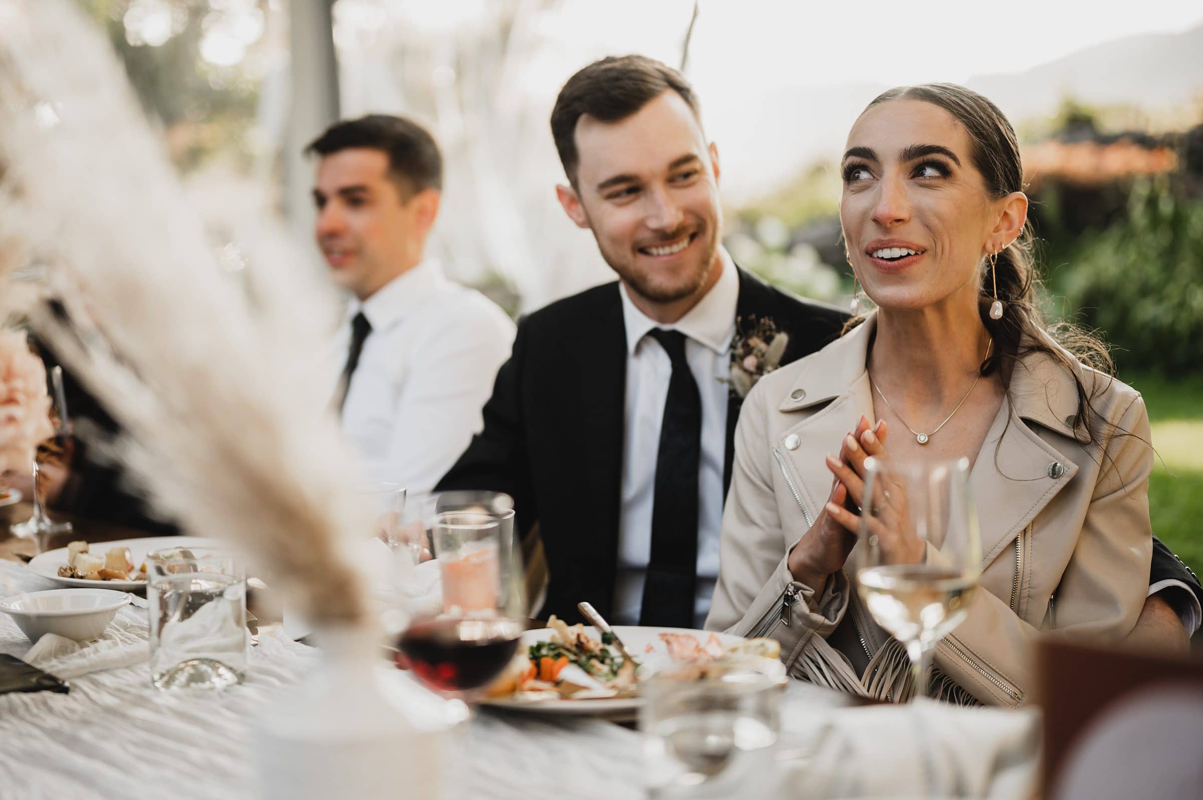 A couple in formal attire sits at an outdoor table, smiling and enjoying a meal with others, creating the perfect moment for wedding photos at The Griffin House.
