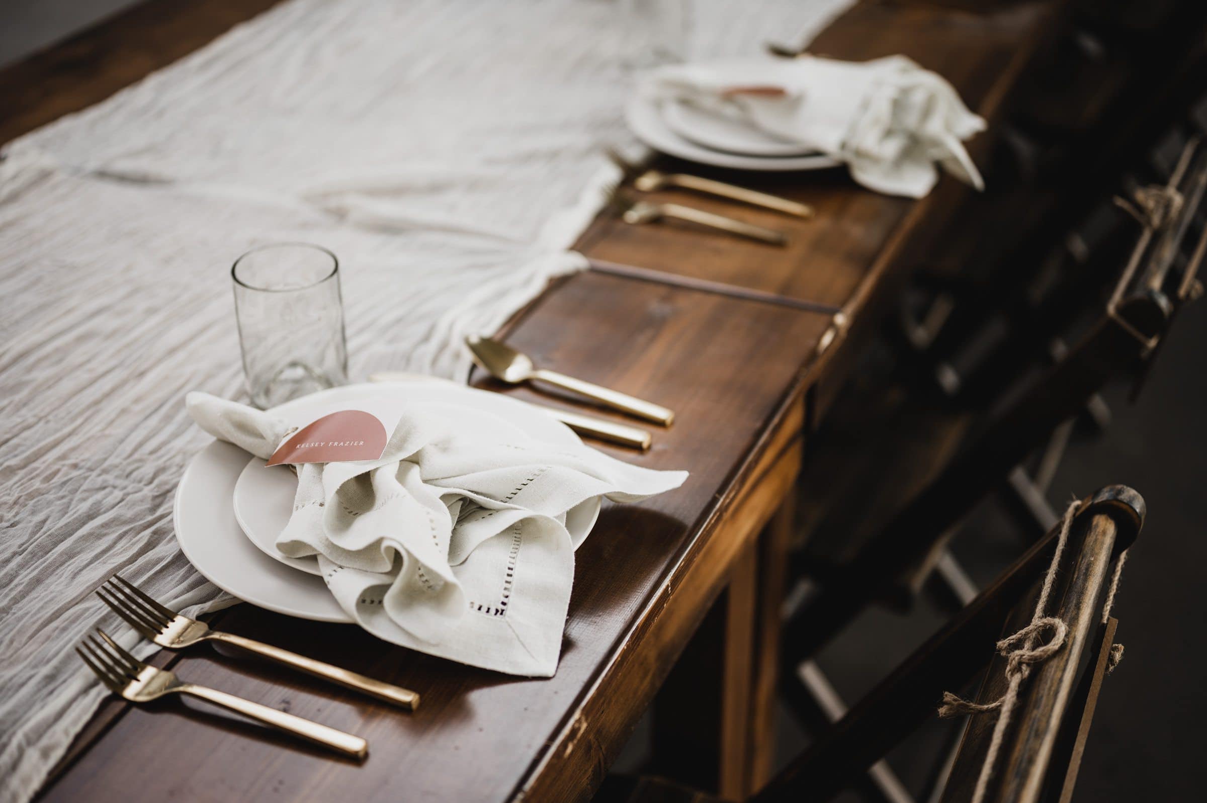 The wooden table set features white plates, gold cutlery, glasses, and cloth napkins, beautifully arranged with a rustic table runner. Perfect for capturing stunning wedding photos at The Griffin House.