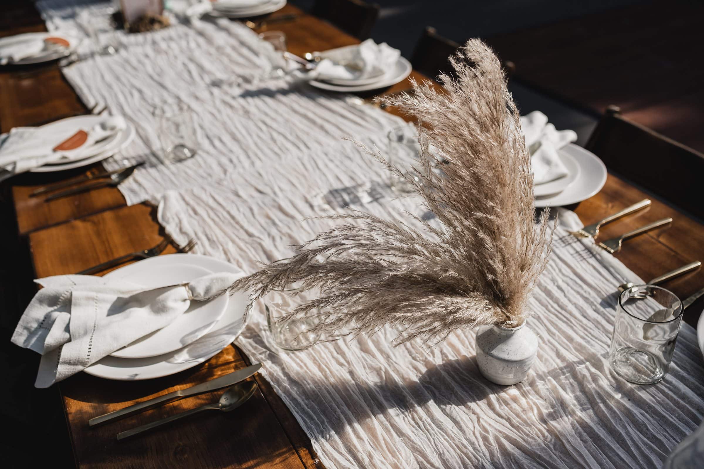 A charming rustic table setting featuring white plates, cloth napkins, and a pampas grass centerpiece on a textured table runner. Perfect for capturing elegant wedding photos at The Griffin House.