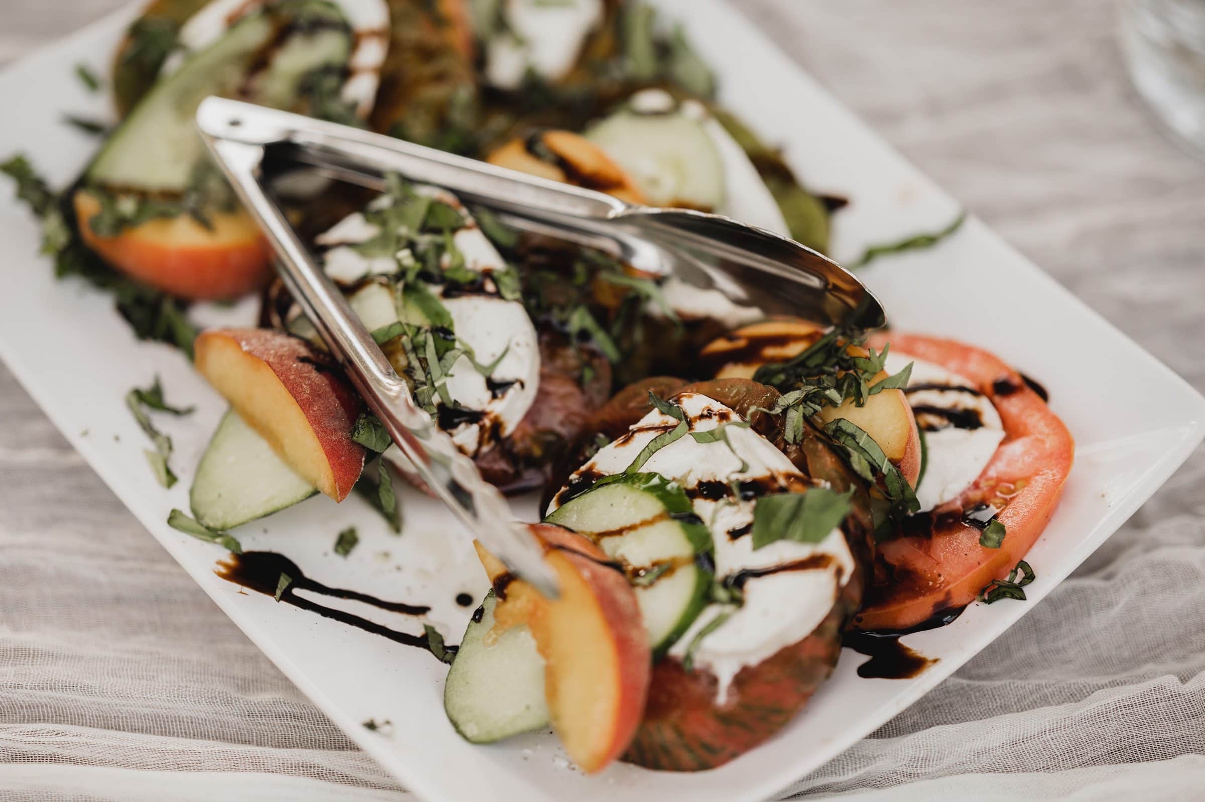 A beautifully arranged Caprese salad featuring sliced tomatoes, mozzarella, peaches, and basil drizzled with balsamic glaze on a white plate—a dish as memorable as wedding photos at The Griffin House.