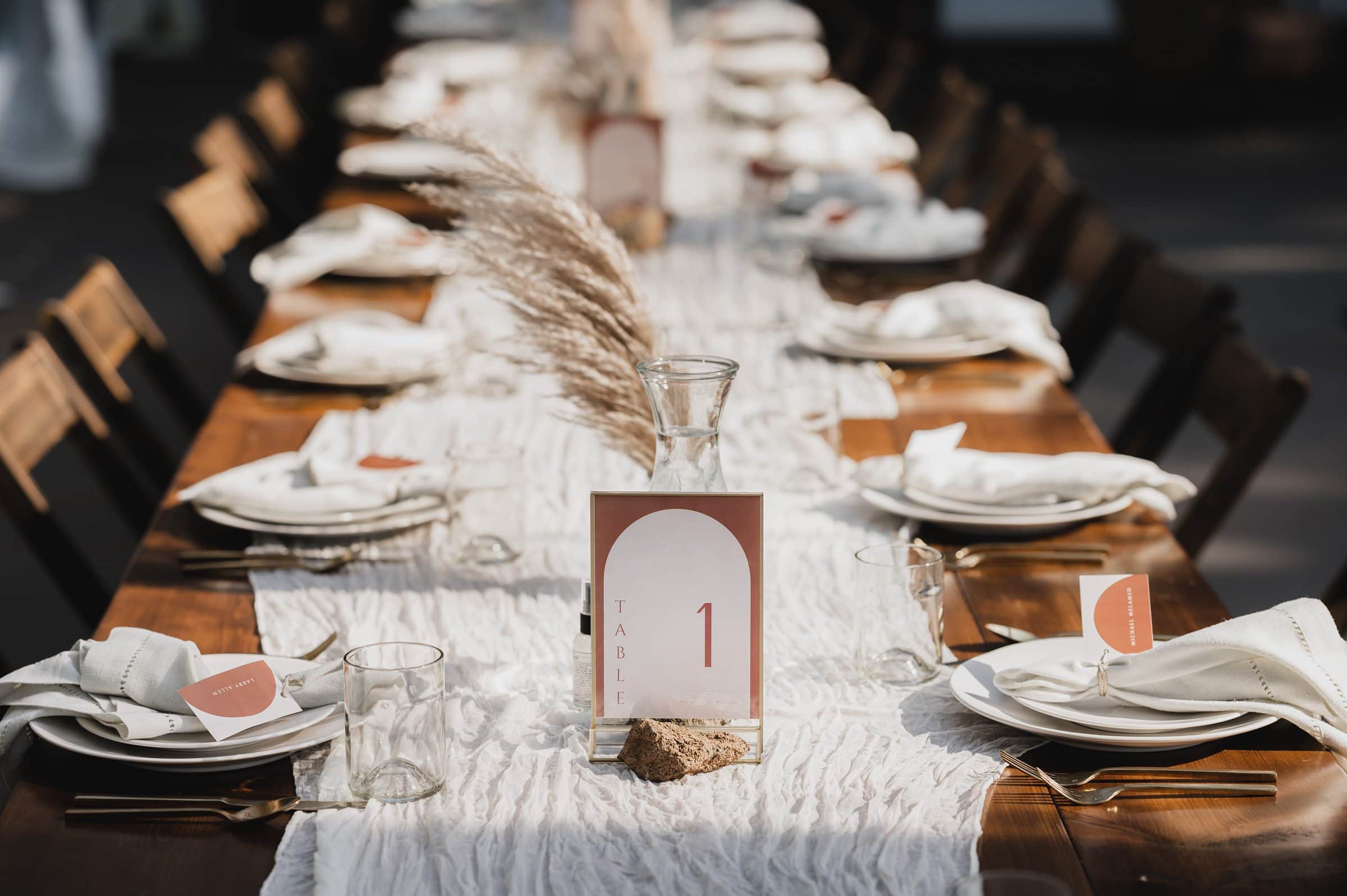 Elegant outdoor table setting with white linens, plates, and glasses. A Table 1 sign and pampas grass centerpiece create a stunning ambiance for wedding photos at The Griffin House.