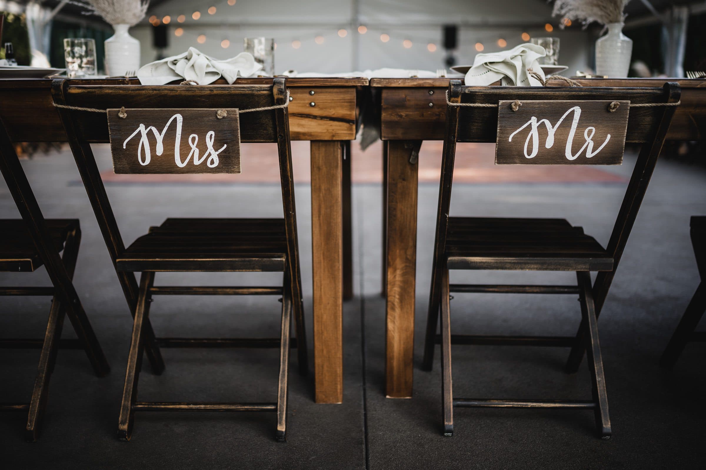 At The Griffin House, wooden chairs labeled Mrs and Mr sit at a rustic wedding reception table with string lights twinkling in the background—perfect for capturing unforgettable wedding photos.
