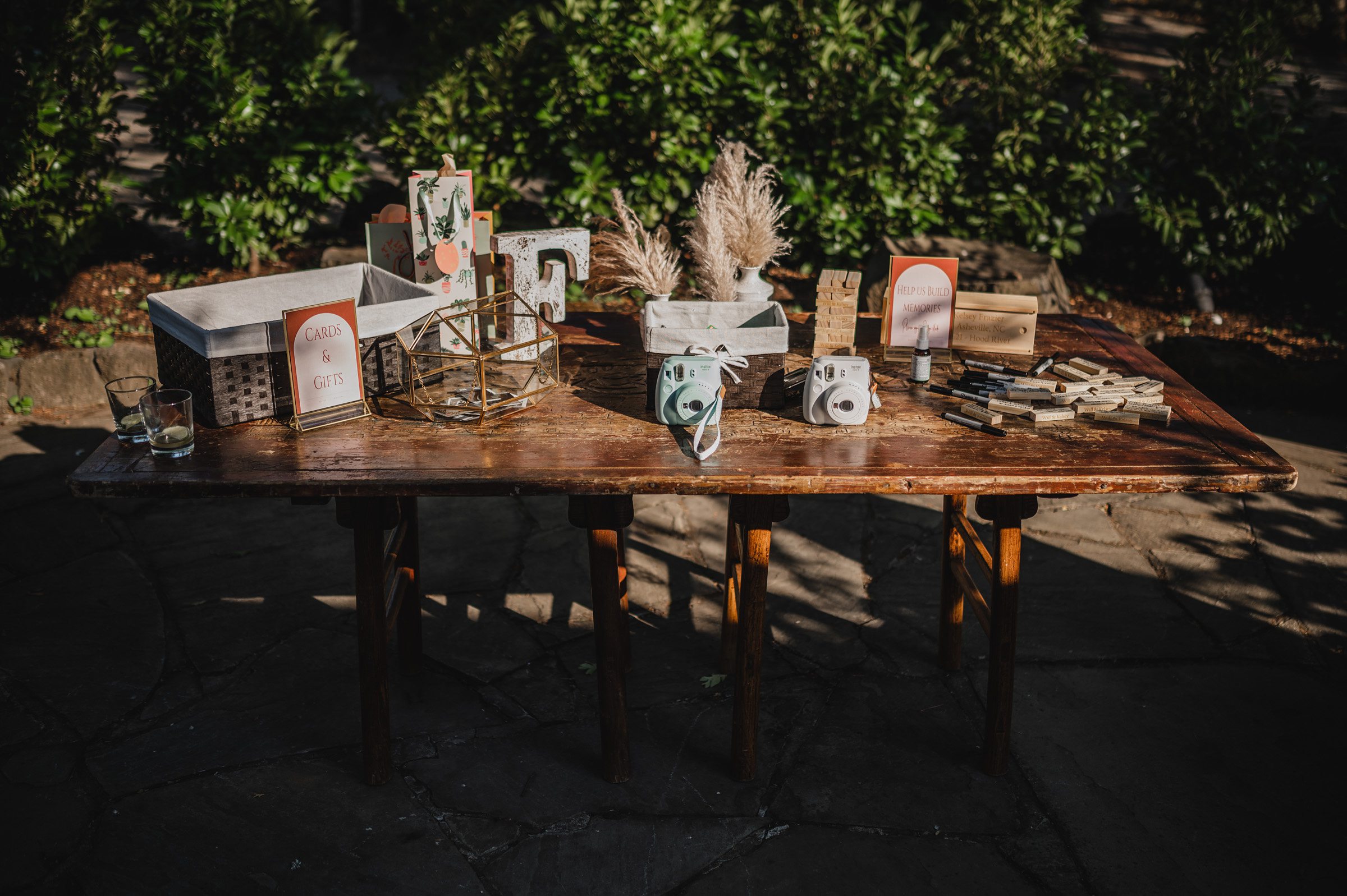 A rustic table adorned with cameras, decorative items, wooden blocks, and cards is set up outside in a garden, perfect for capturing wedding photos at The Griffin House.