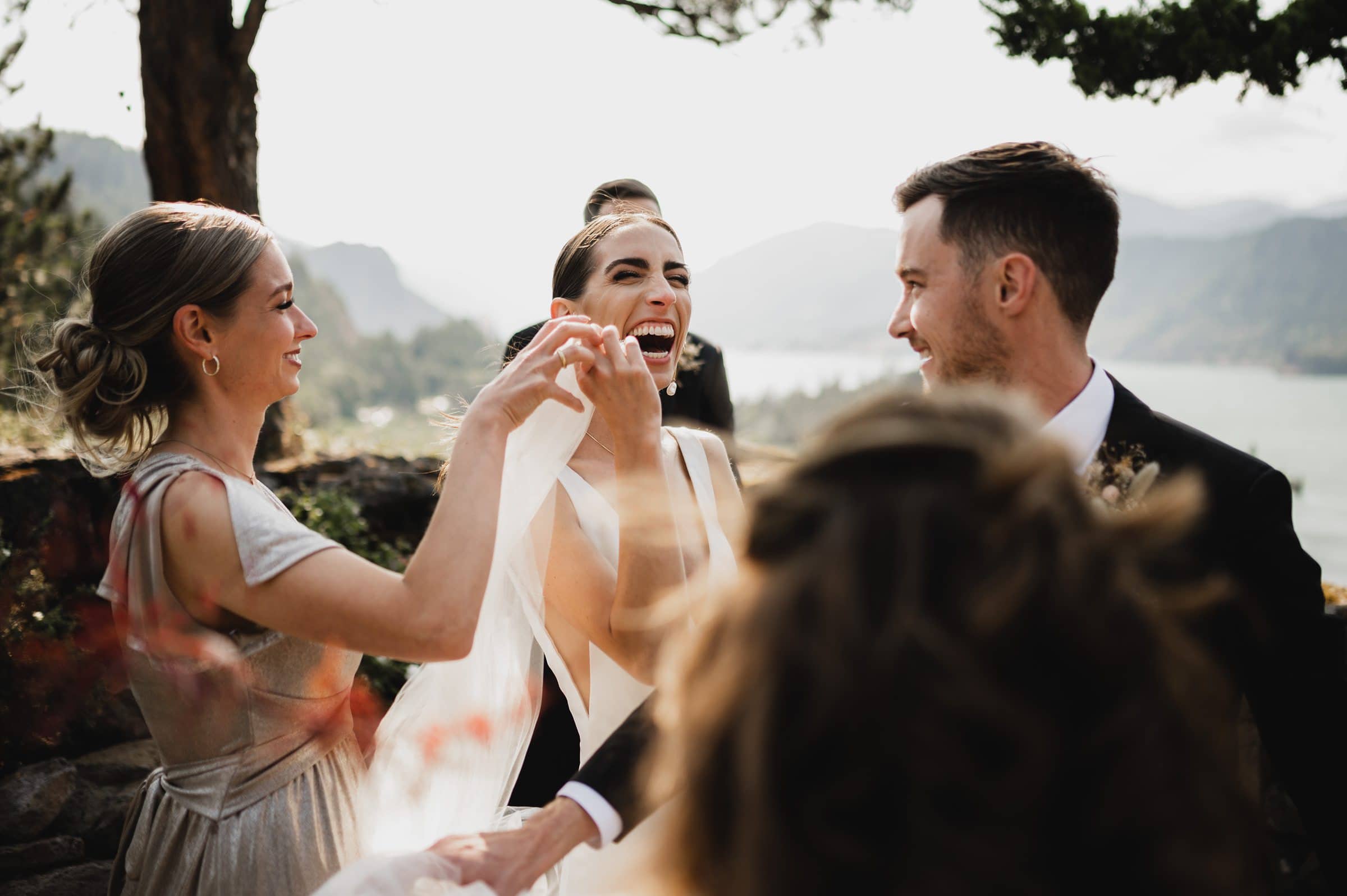 Bride laughing with bridesmaid and groom against a scenic mountain backdrop, capturing beautiful wedding photos at The Griffin House.
