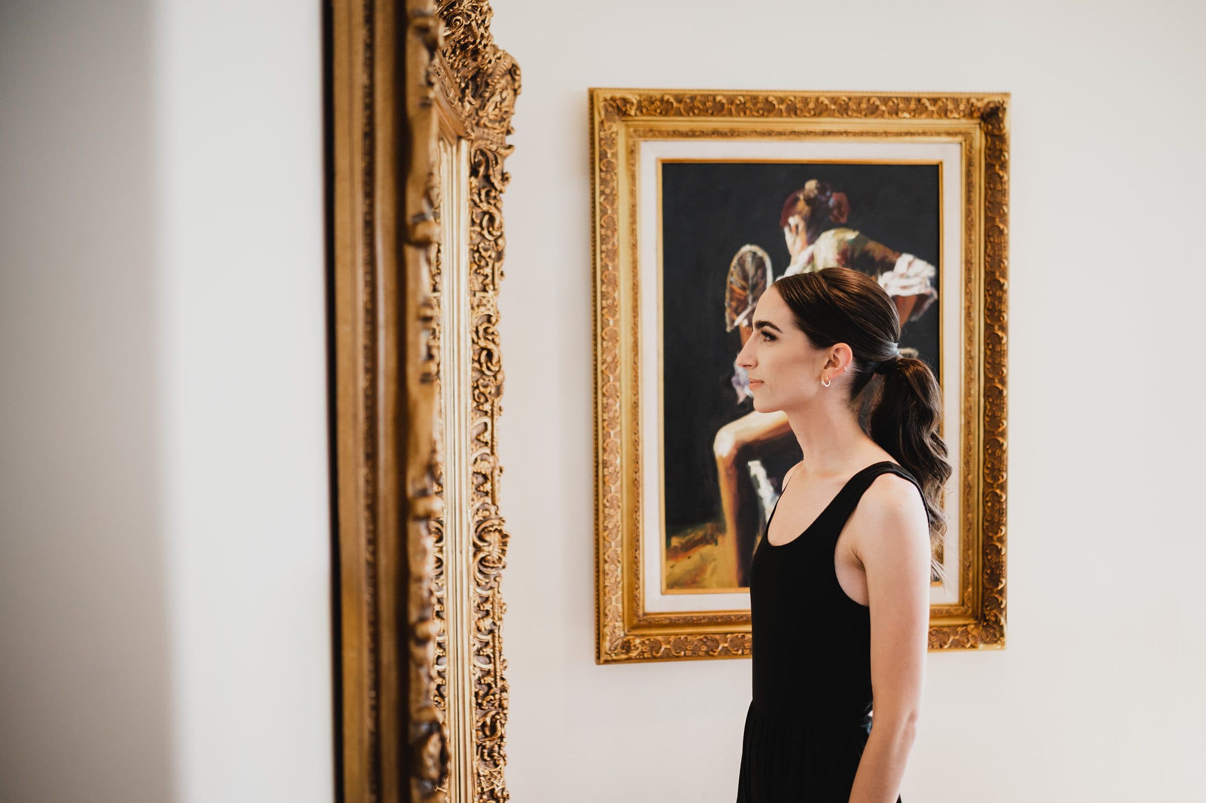 A woman in a black dress admires a framed painting in an art gallery, capturing a moment as timeless as wedding photos at The Griffin House.