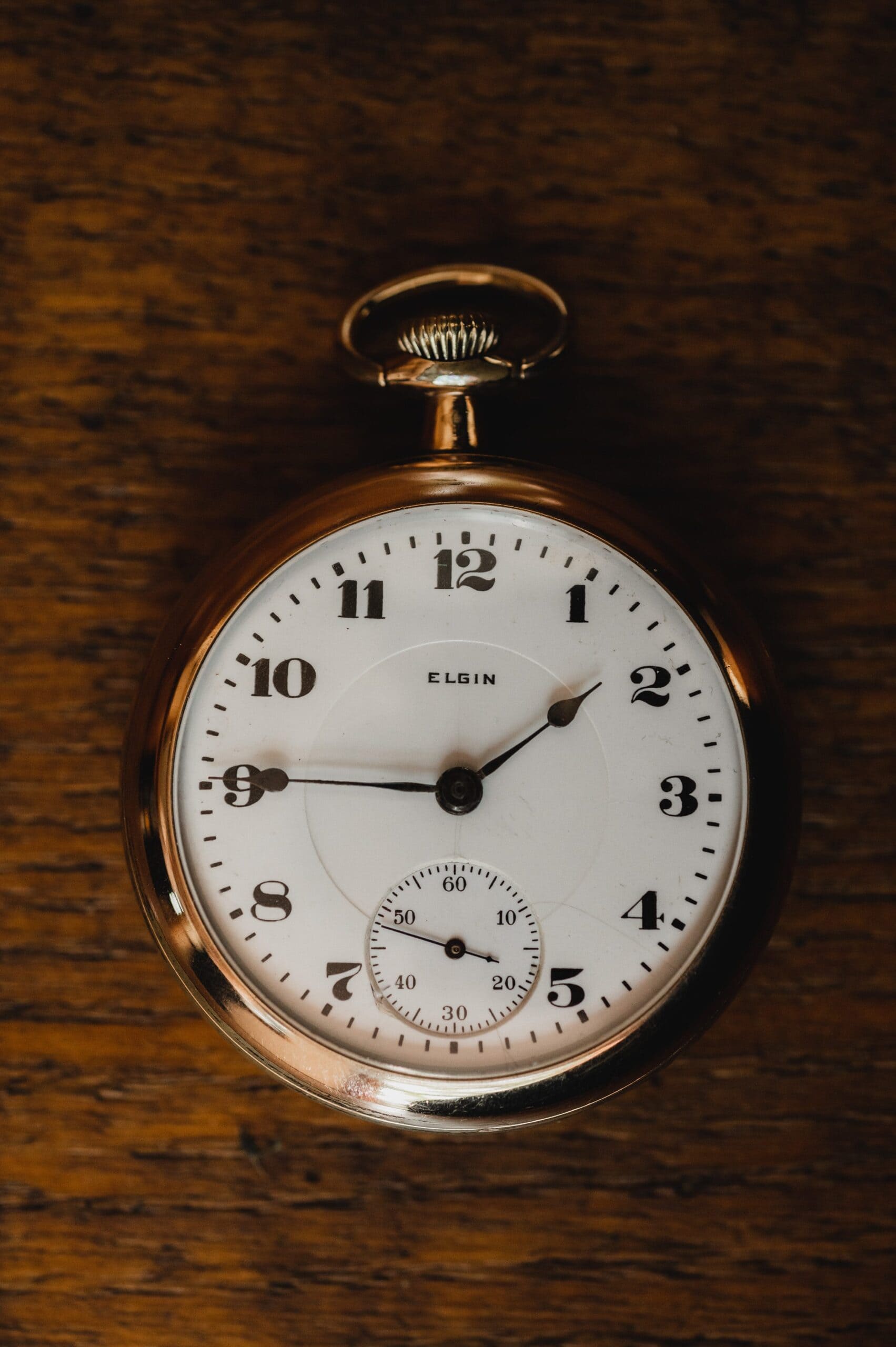 A vintage Elgin pocket watch with a white face and black numbers is elegantly placed on a wooden surface, capturing the timeless charm perfect for wedding photos at The Griffin House.