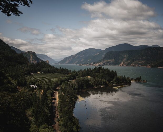The Columbia River flows through a lush valley with forested hills and majestic mountains under a cloudy blue sky, as view at a wedding photographed at The Griffin House.