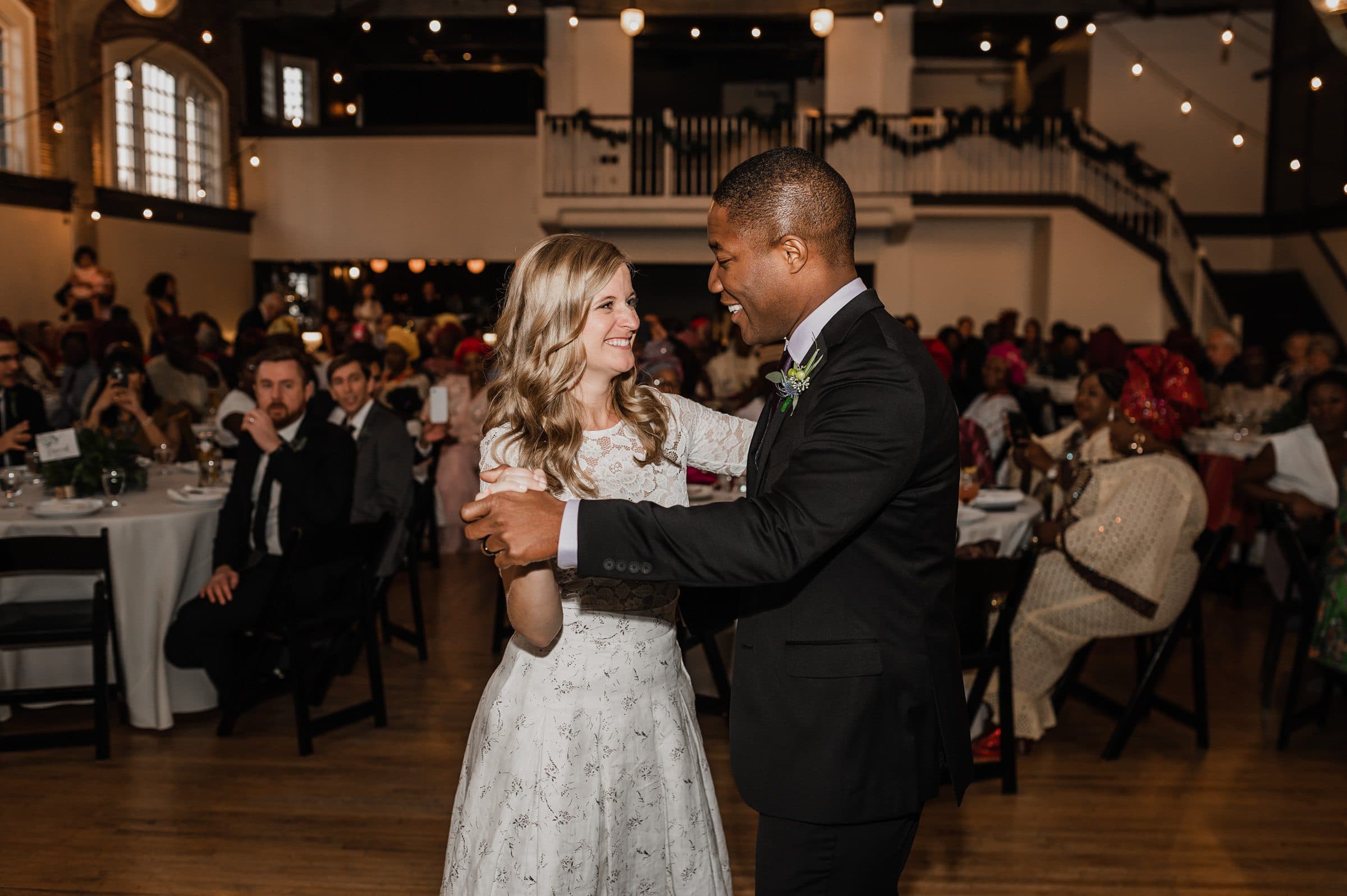 At The Evergreen, a renowned Portland wedding venue, the bride and groom dance joyfully at their reception, surrounded by seated guests in a warmly lit setting.