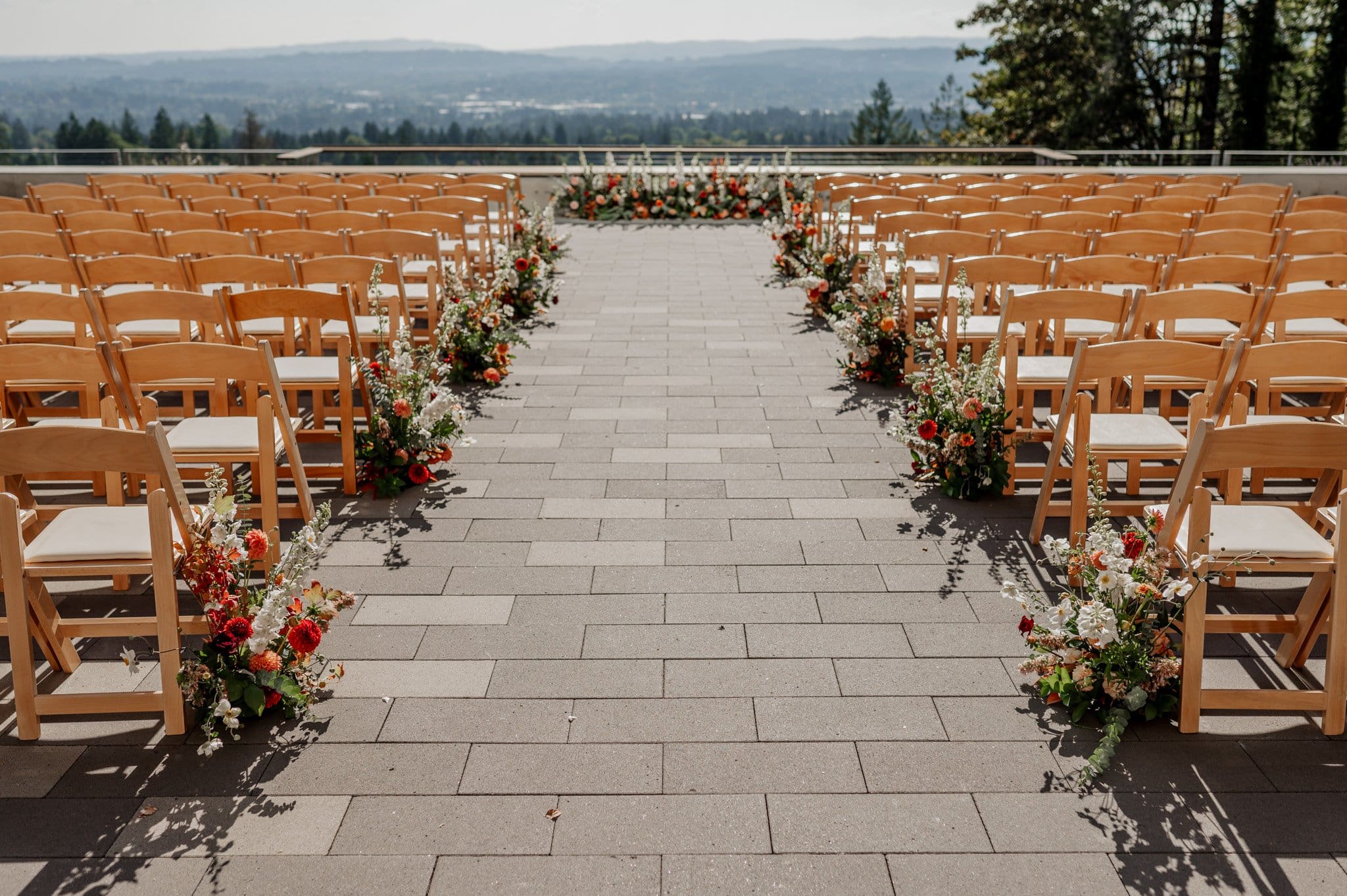 An outdoor wedding setup at Amaterra Winery features rows of wooden chairs and elegant floral arrangements lining a stone aisle, all overlooking a scenic view that makes this Portland wedding venue truly enchanting.