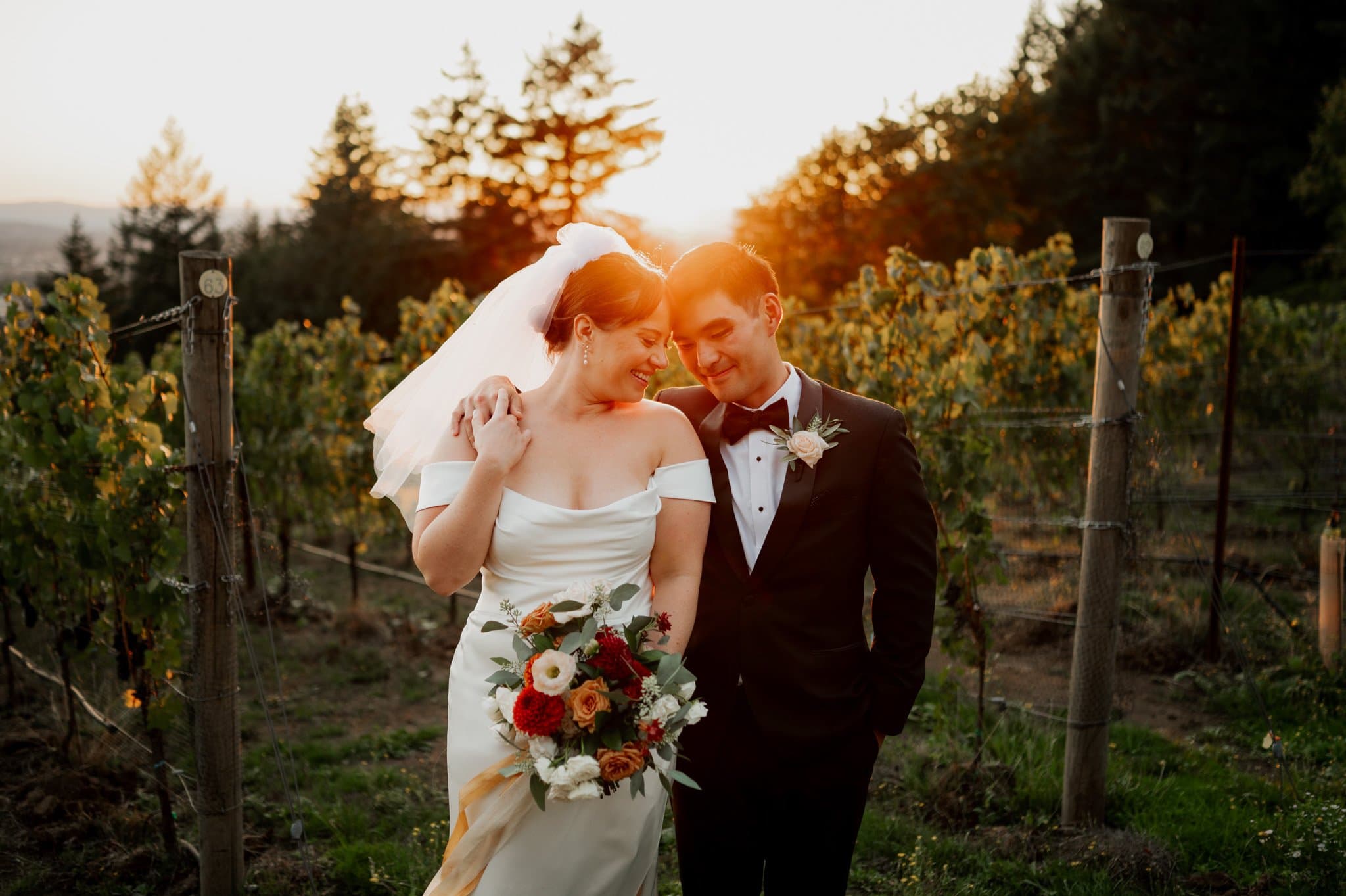 Bride and groom smiling at each other in the warm glow of sunset at Amaterra Winery, a picturesque Portland wedding venue, with the bride holding a bouquet of flowers.