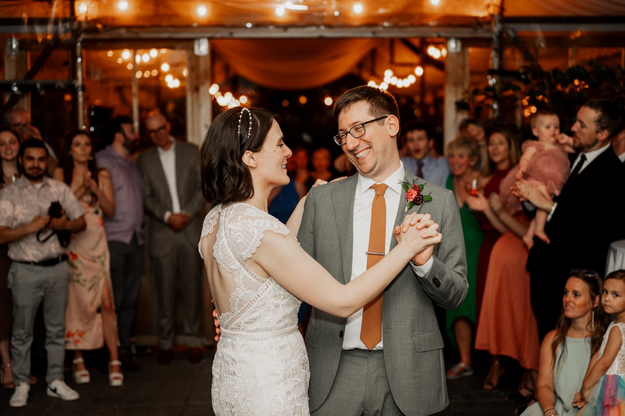 A couple dances joyfully at their wedding reception at Blockhouse, a Portland wedding venue, surrounded by smiling guests under warm string lights.