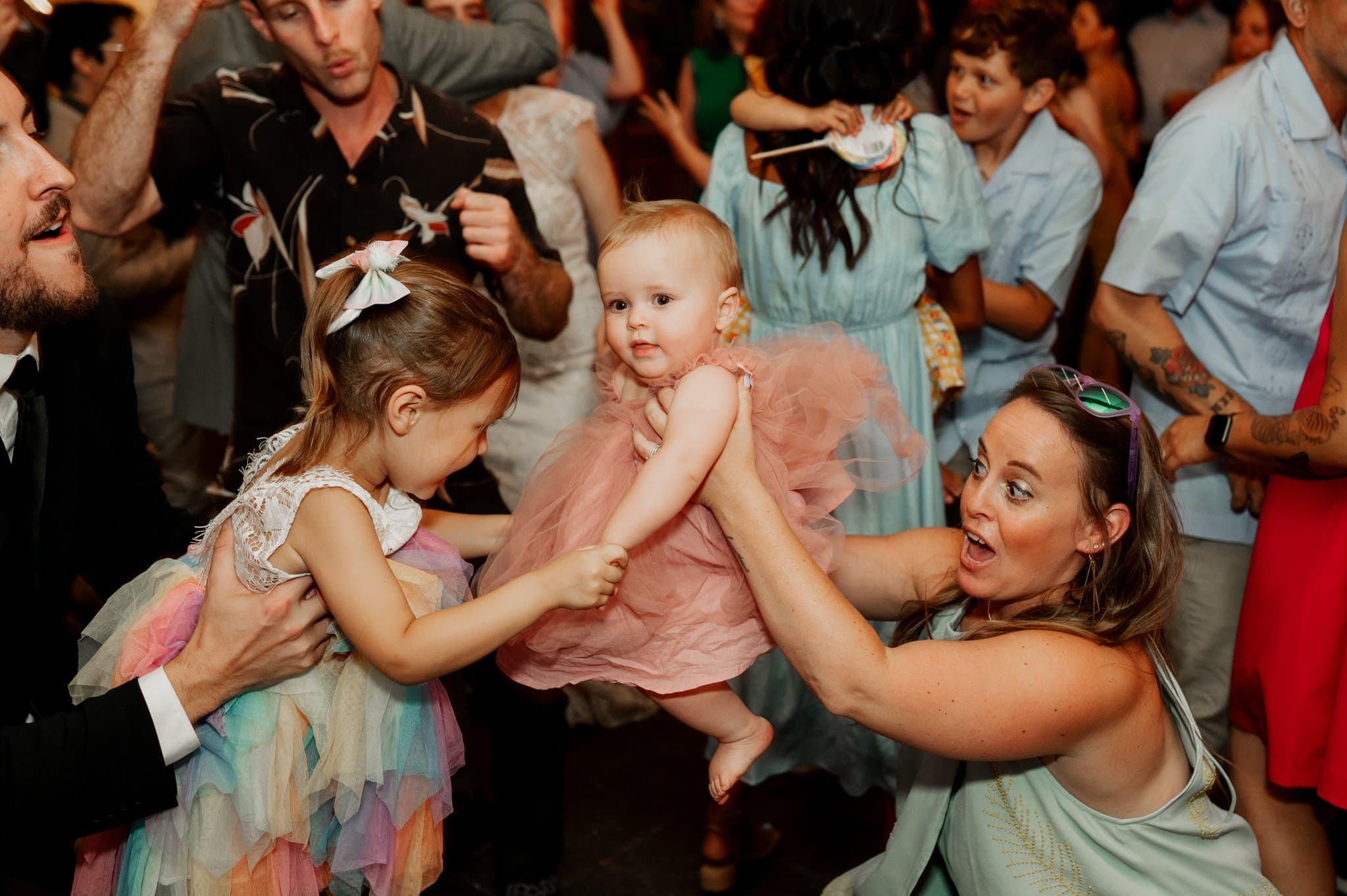 Adults and children in colorful outfits dance and play joyfully at a lively wedding gathering, capturing memorable moments akin to wedding photos at Blockhouse.