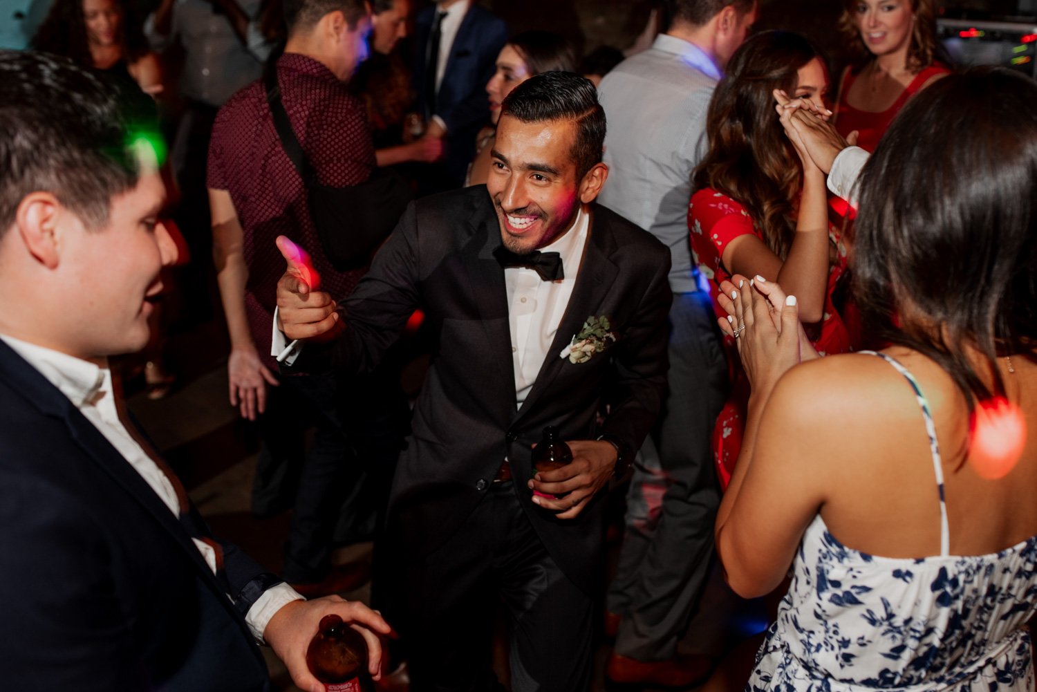 Guests in formal attire twirl and laugh under vibrant, colorful lights at a Leach Botanical Garden wedding, creating a lively and unforgettable atmosphere.
