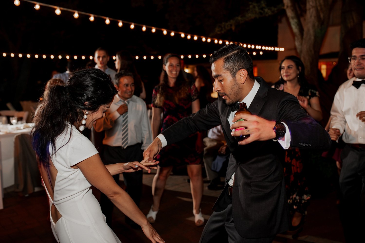 Under the warm glow of string lights, guests dance at an outdoor party during a Leach Botanical Garden wedding.