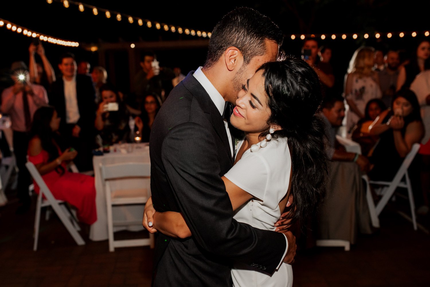 A couple embraces while dancing at a Leach Botanical Garden wedding, with smiling guests enjoying the moment in the background.