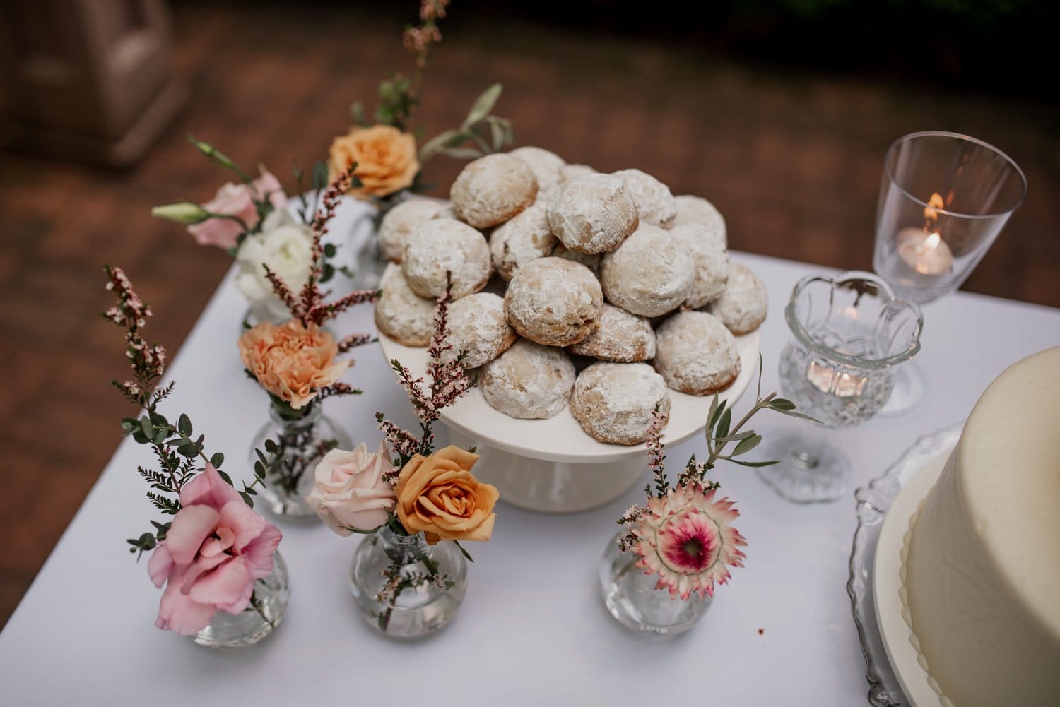 Powdered cookies are displayed on a stand, surrounded by small flower vases on a table.