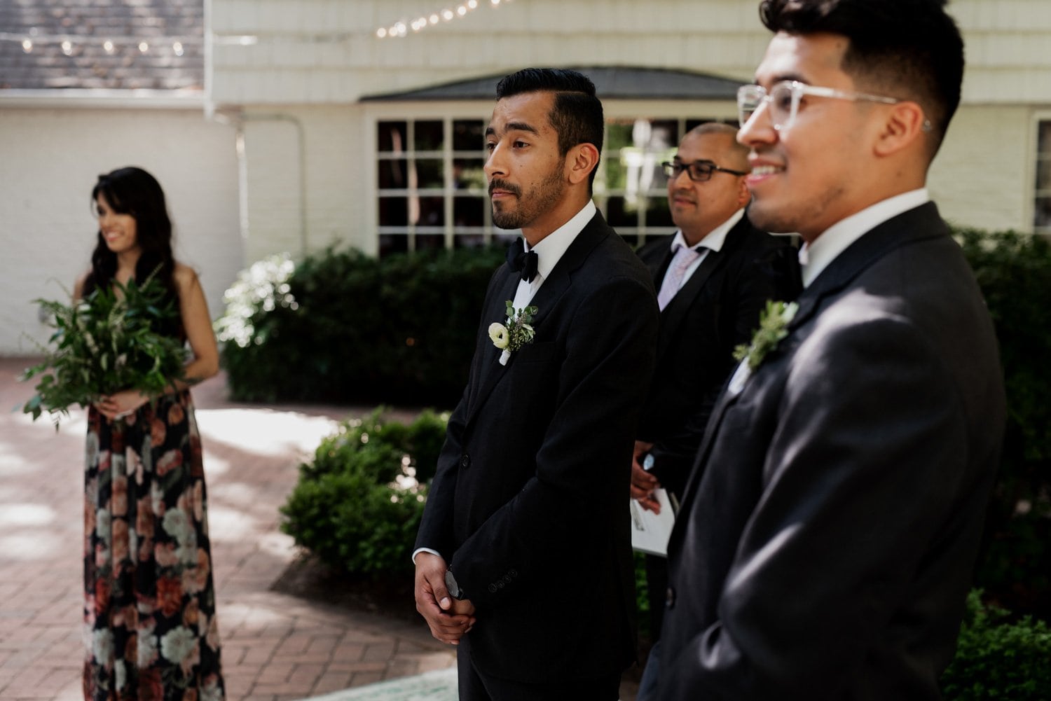 A groom stands with groomsmen and a bridesmaid in the lush setting of Leach Botanical Garden, surrounded by greenery and vibrant foliage.